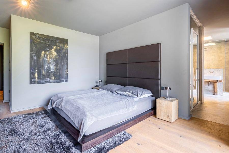Schlafzimmer mit großem Bett, Teppich und Zugang zu einem modernen Bad mit Glaswand.