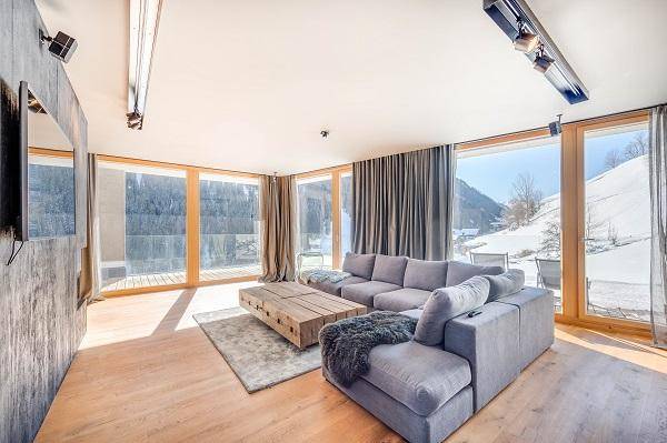 Helles Wohnzimmer mit großem Sofa, Holzboden und raumhohen Fenstern mit Bergblick.