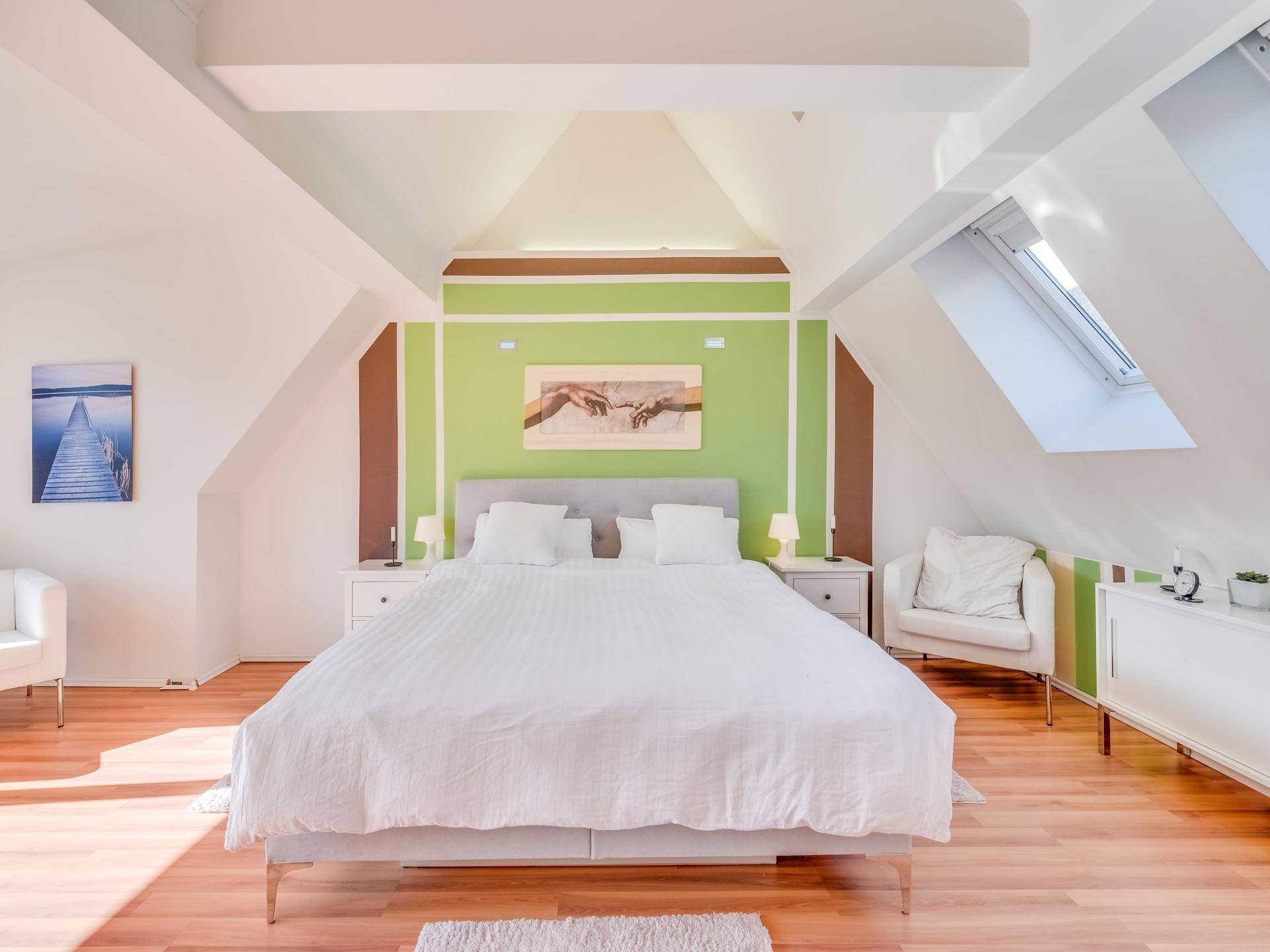 Helles Schlafzimmer im Dachgeschoss mit Holzboden, Dachfenster und farbiger Akzentwand.