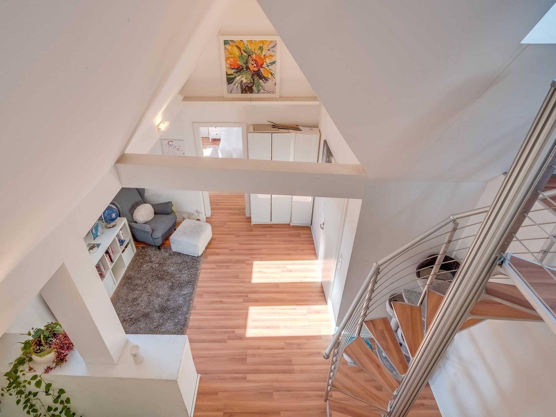 Heller offener Loftbereich mit Holzfußboden, Dachschrägen und moderner Wendeltreppe.