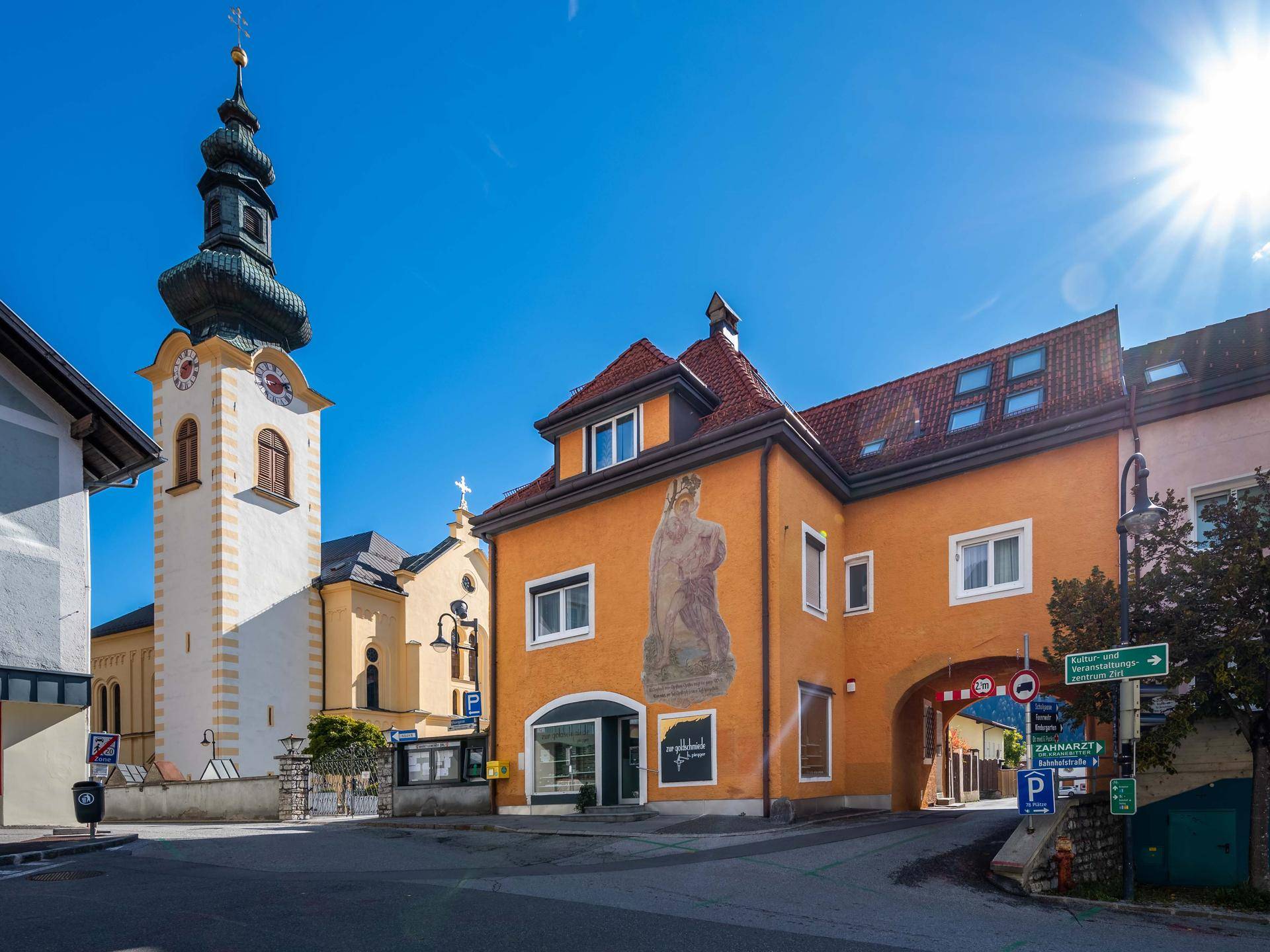 Historisches Gebäude mit farbenfroher Fassade und angrenzender Kirche unter blauem Himmel.