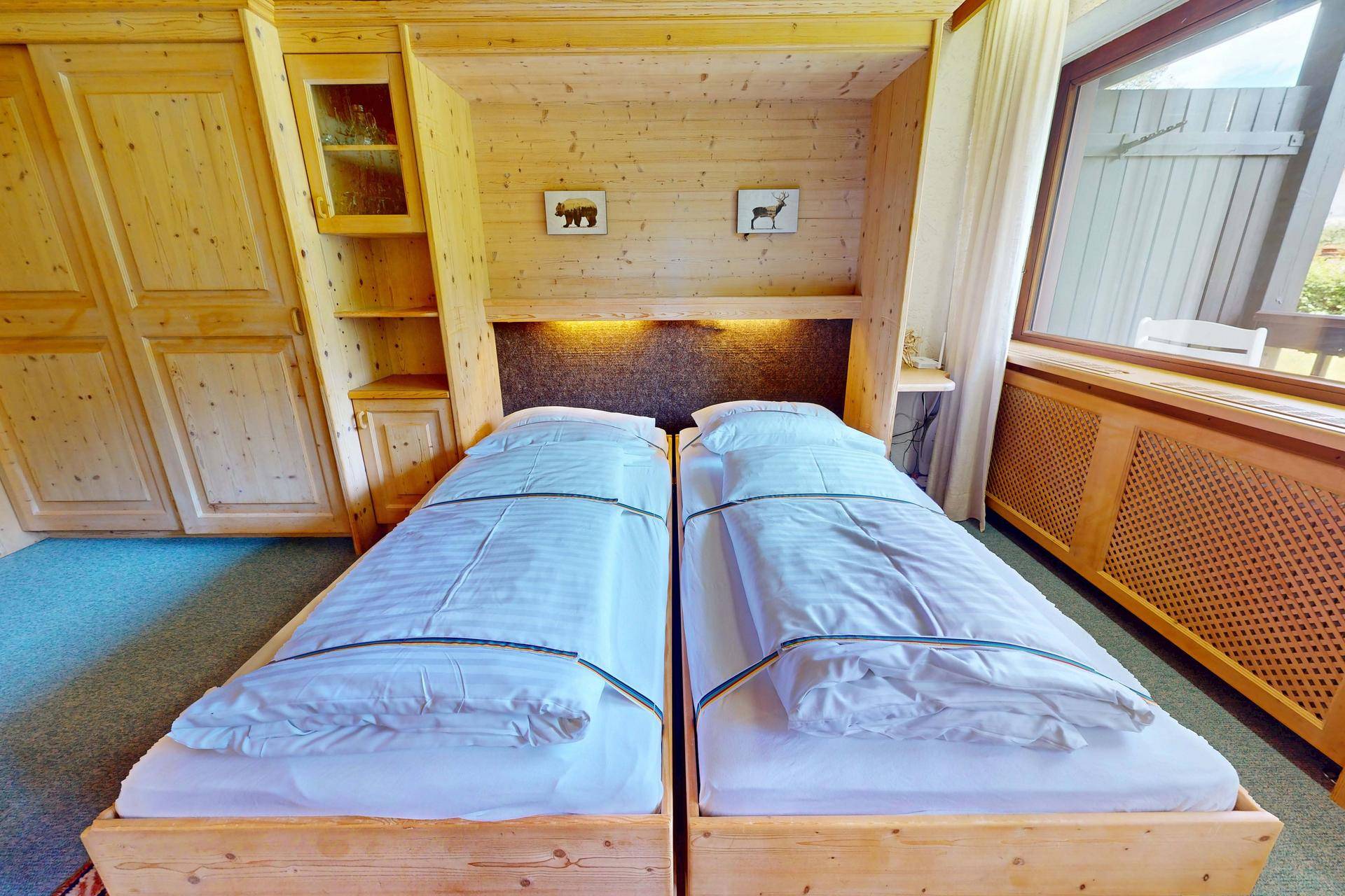 Helles Schlafzimmer mit zwei Einzelbetten, Holzmöbeln und Blick nach draußen.