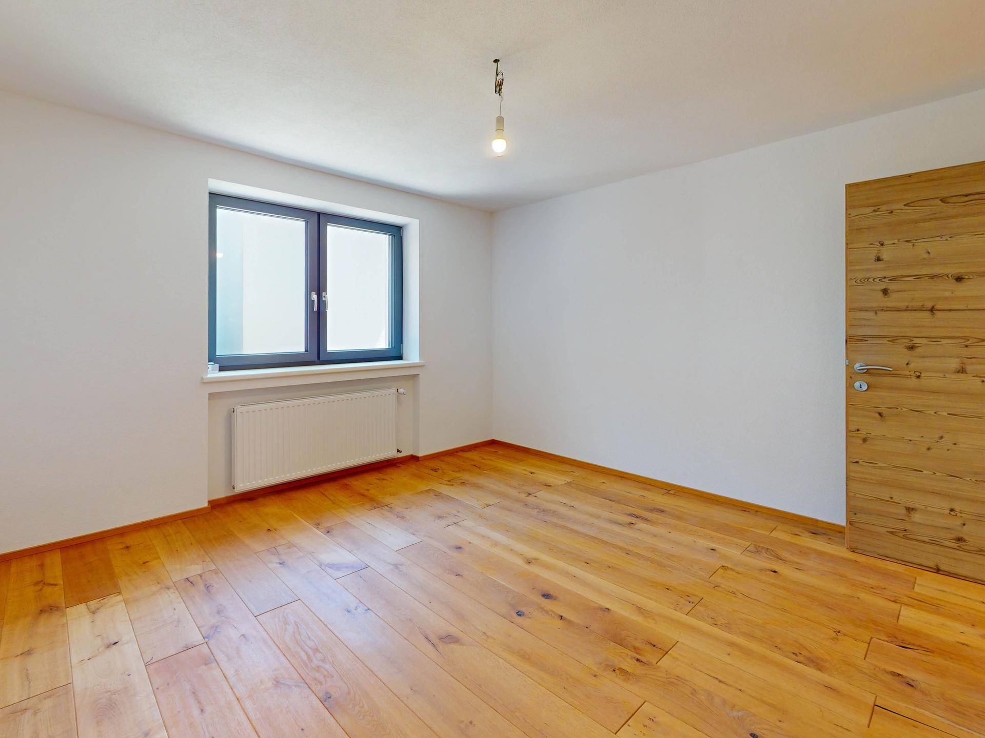 Gemütliches Schlafzimmer mit Holzboden und einem großen Fenster, das viel Tageslicht hereinlässt.