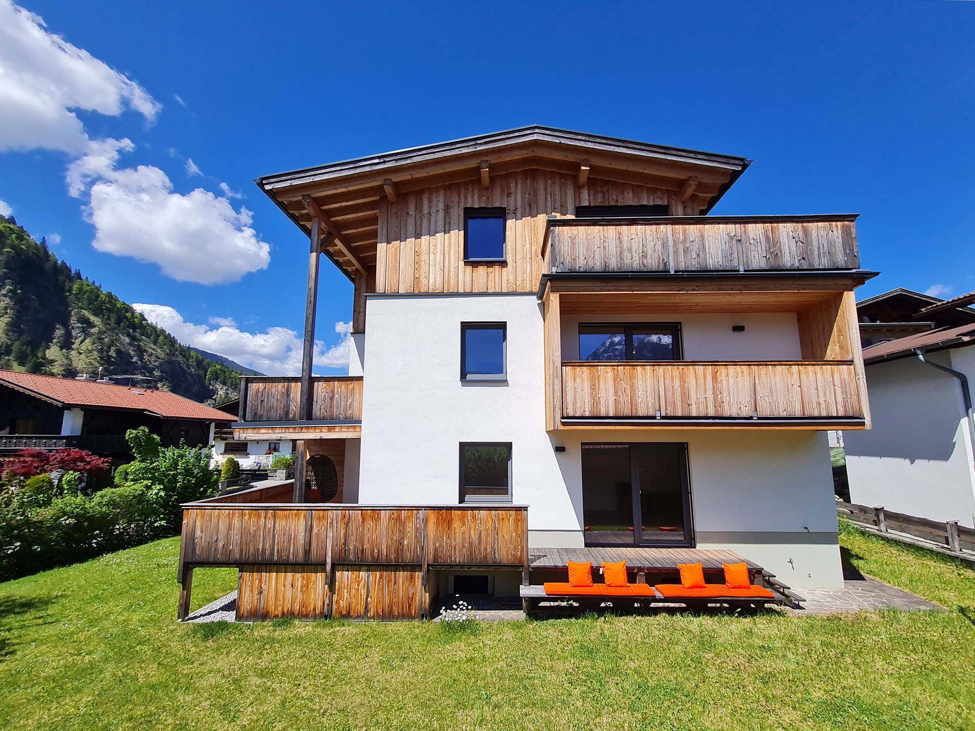Modernes Wohnhaus mit Holzfassade, Balkonen und einem gepflegten Rasen in alpiner Umgebung.