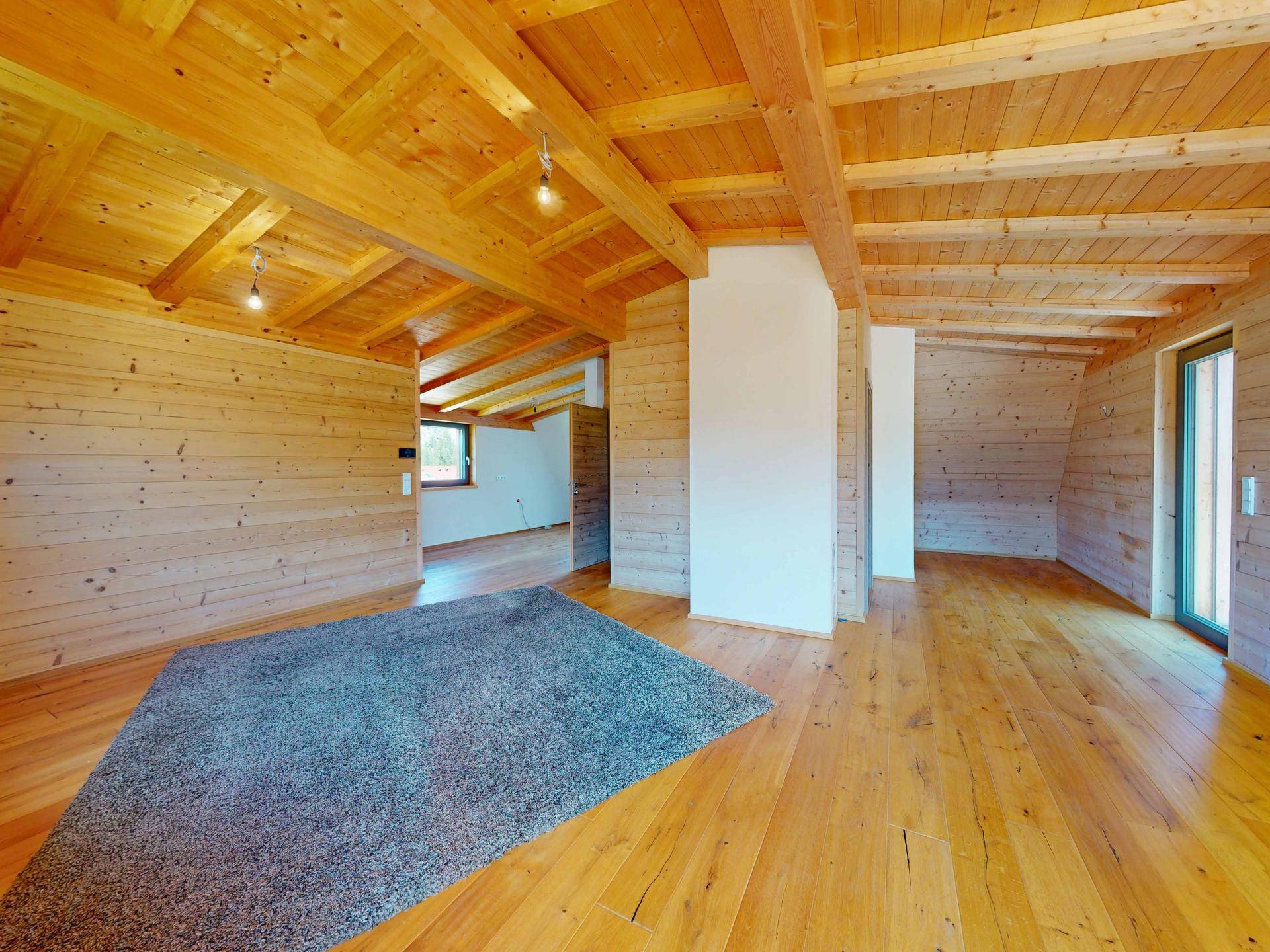 Heller Raum mit Holzböden und -wänden, sichtbaren Deckenbalken und viel natürlichem Licht.