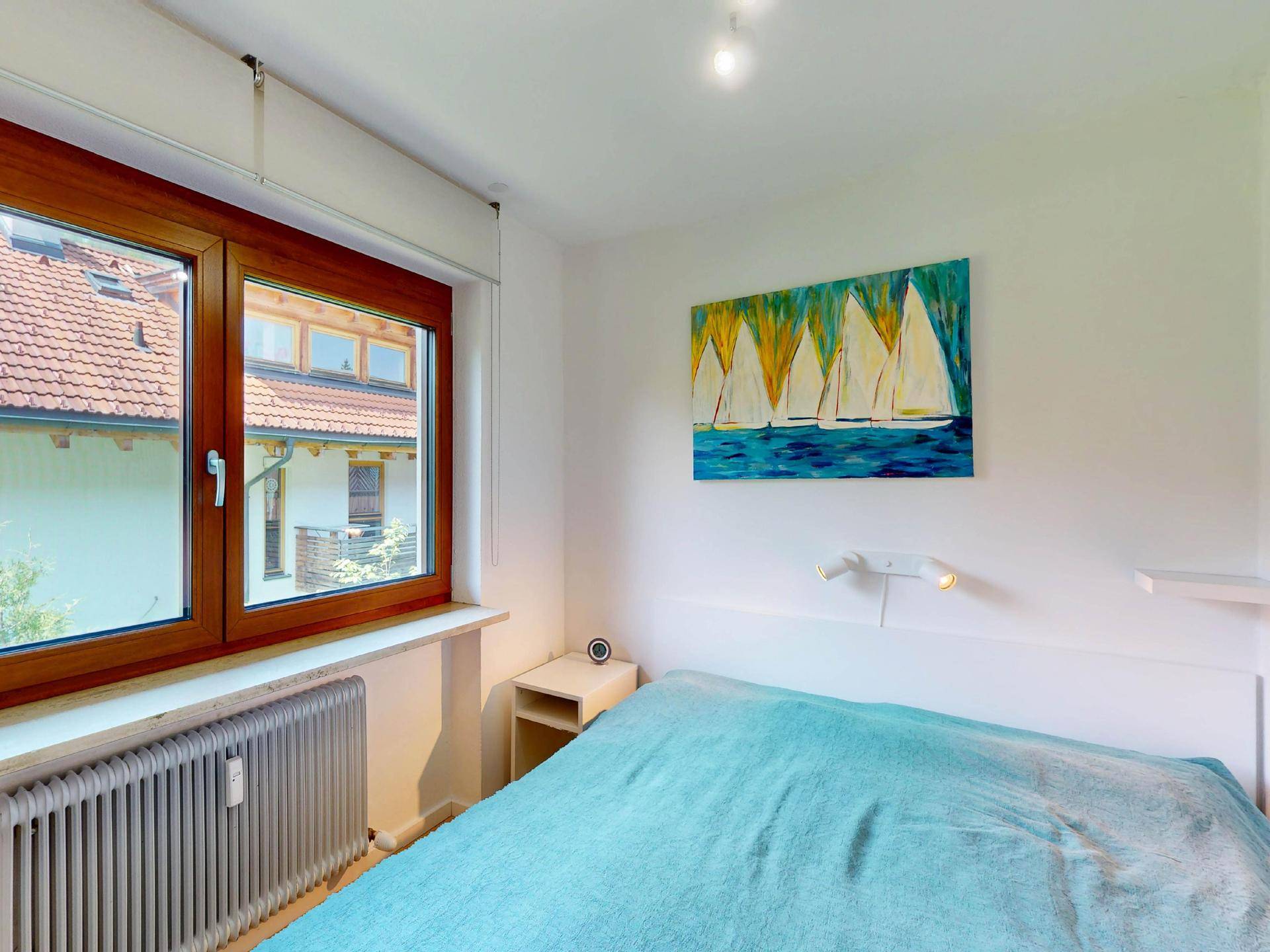 Helles Schlafzimmer mit Holzbett, Nachttisch und Fenster mit Blick auf die Dächer.