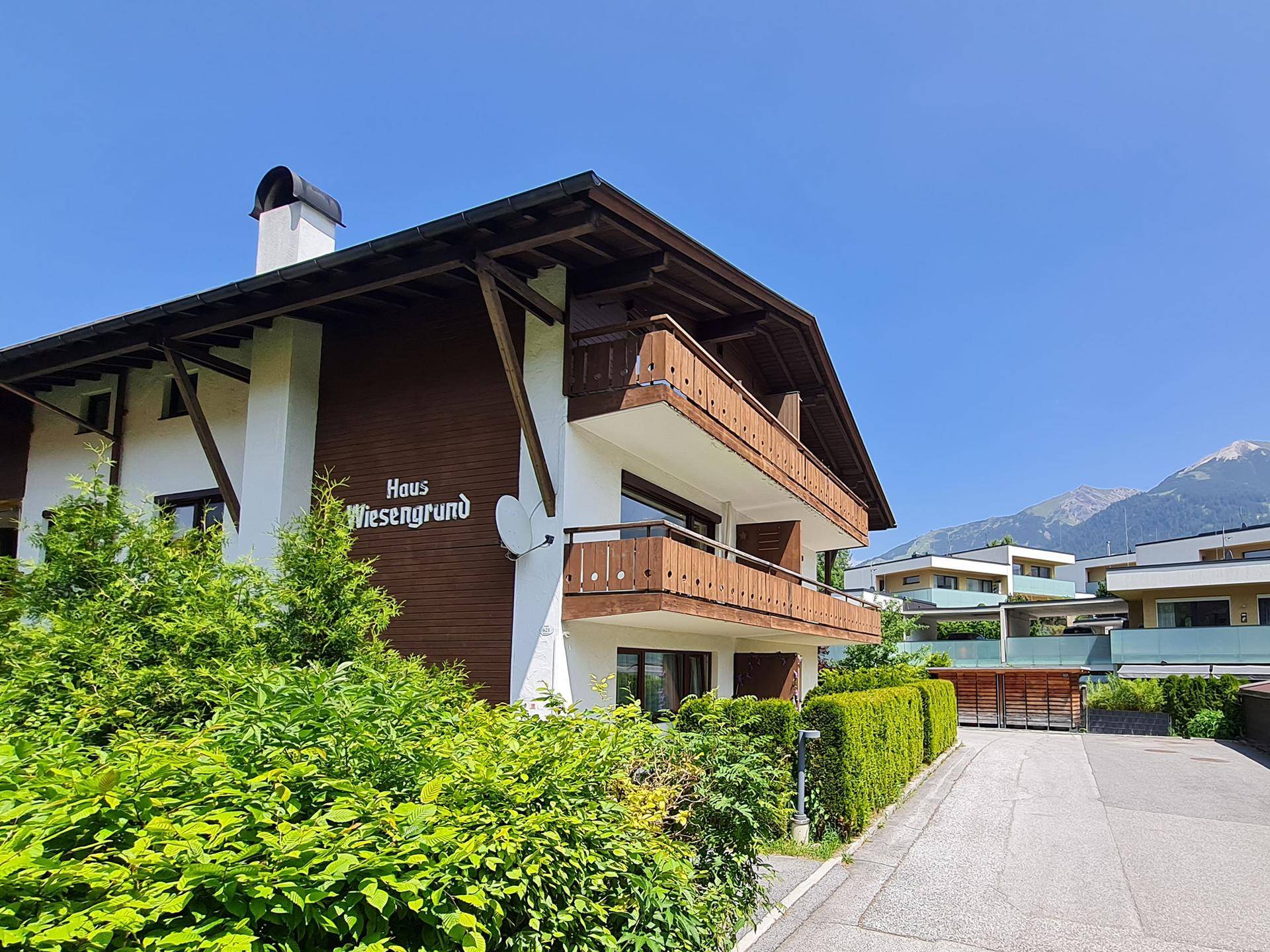 Traditionelles Haus mit Holzfassade, Balkonen und gepflegter Hecke im Vordergrund.