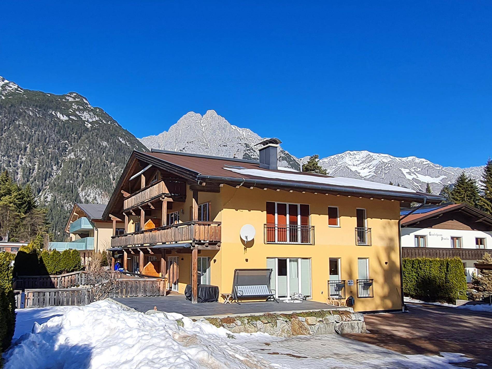 Attraktives Gebäude in alpiner Architektur mit Balkonen und beeindruckendem Bergblick im Winter.