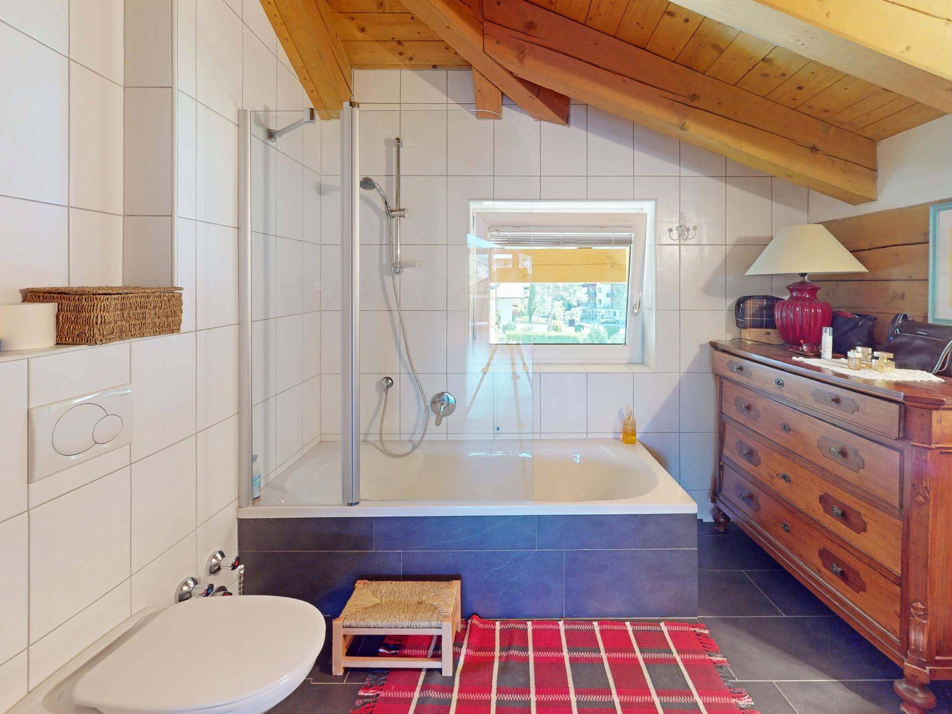 Helles Badezimmer mit Badewanne, Duschabtrennung, Fliesenboden und Dachschräge.