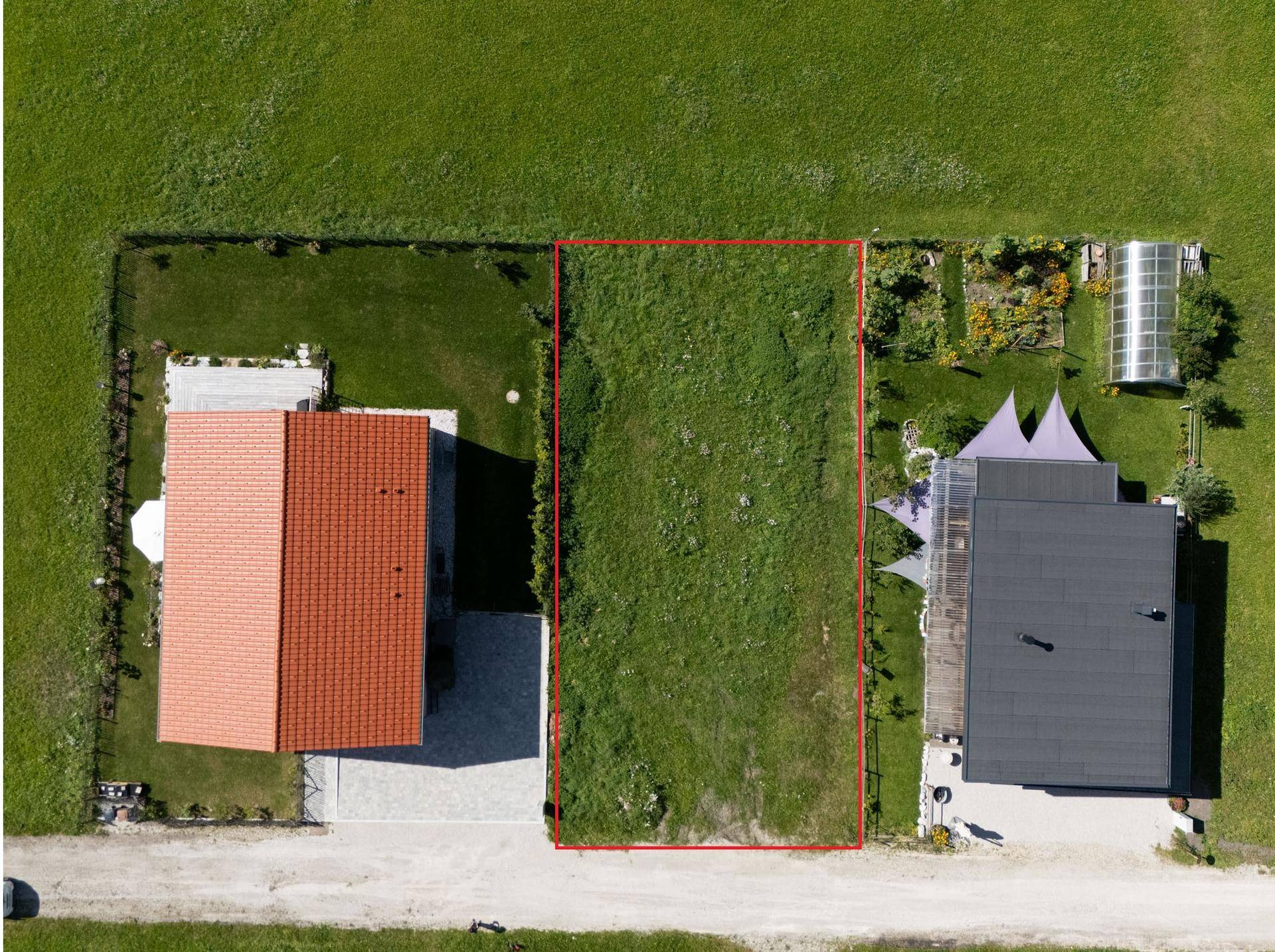 Luftaufnahme eines rechteckigen Baugrundstücks, rot umrandet, zwischen zwei Häusern mit Gärten.