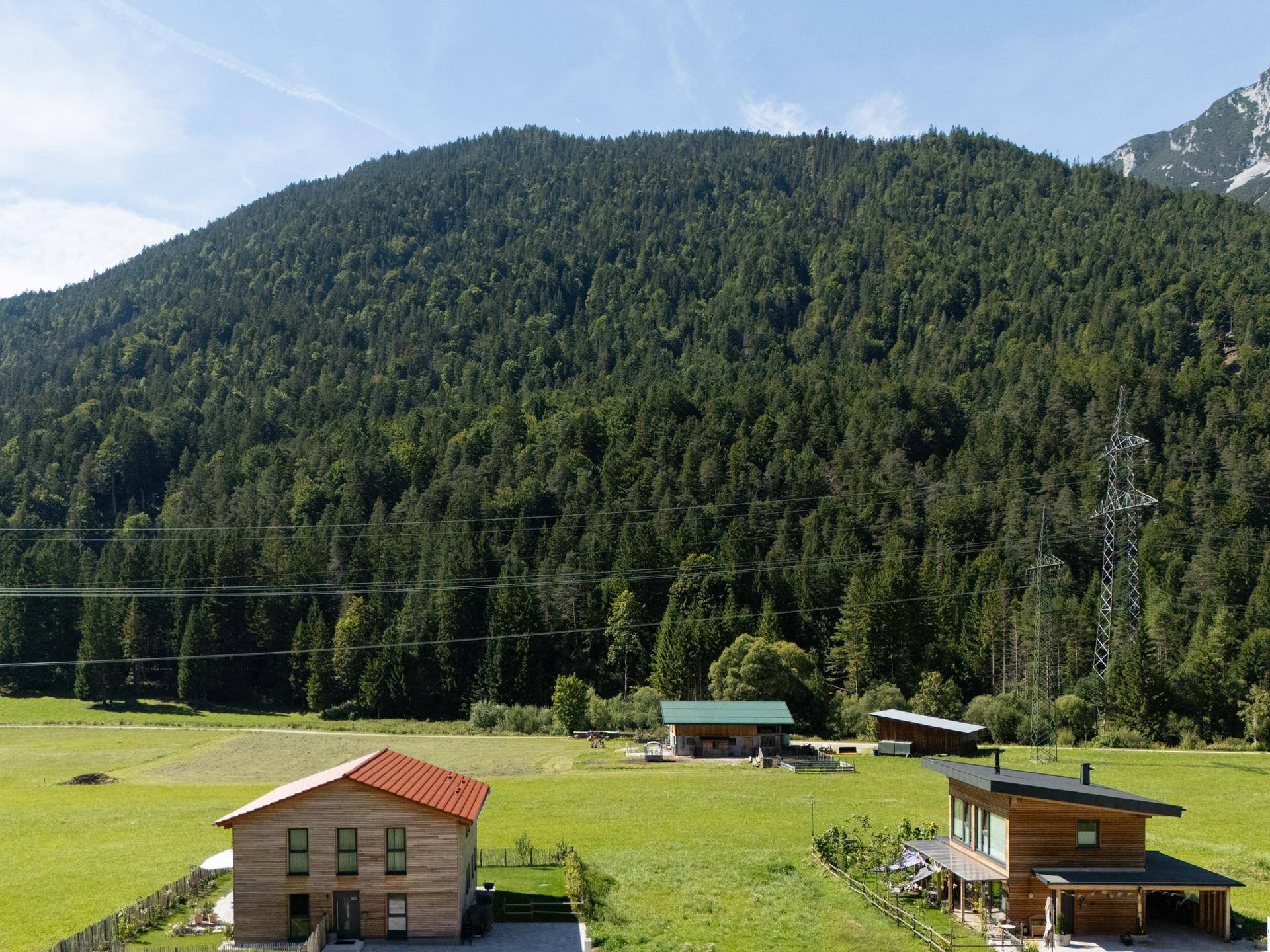 Häuser in einer grünen Tallandschaft mit einem dicht bewaldeten Berg im Hintergrund unter blauem Himmel.