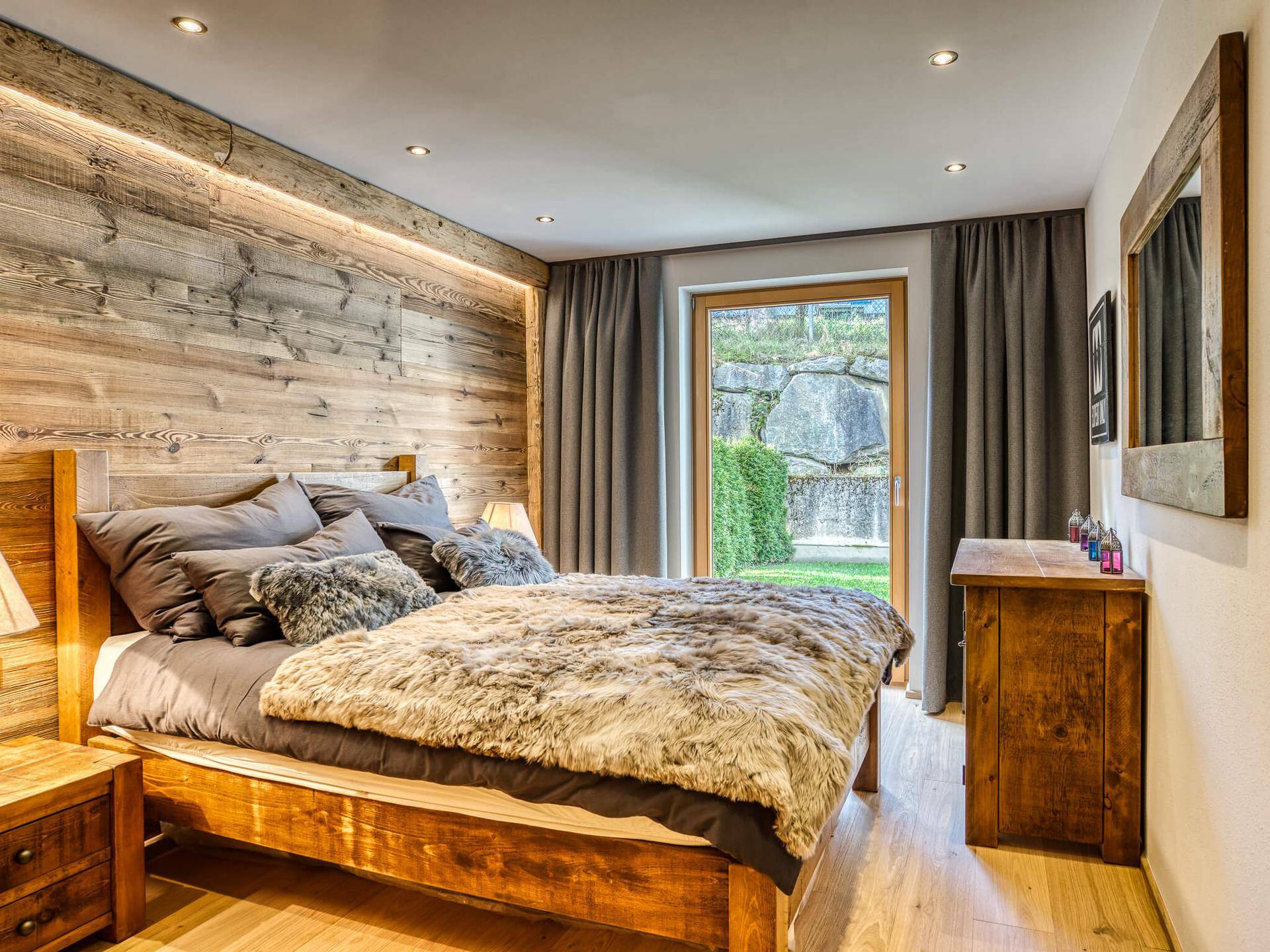 Schlafzimmer mit Holzbett, Holzwandverkleidung und direktem Zugang zu einer kleinen Grünfläche.