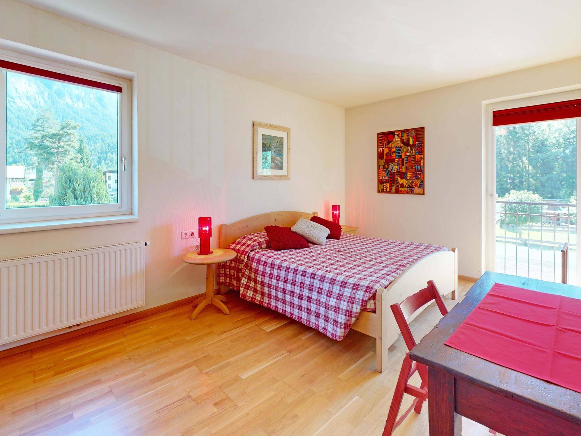 Gemütliches Schlafzimmer mit Holzboden, roten Akzenten und Fenster mit Bergblick.