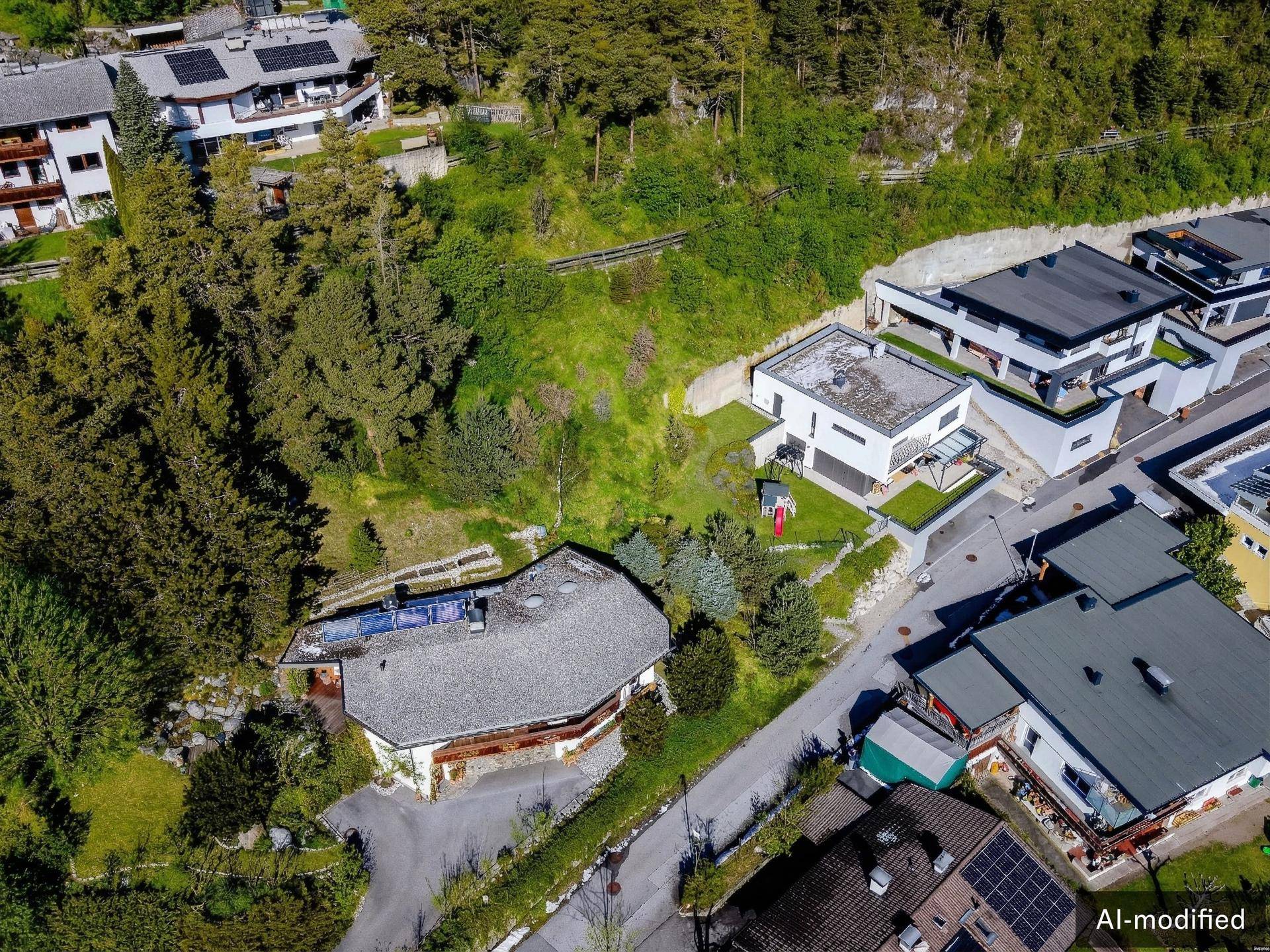 Luftaufnahme einer Wohnsiedlung mit Häusern, viel Grün und Bergen im Hintergrund.