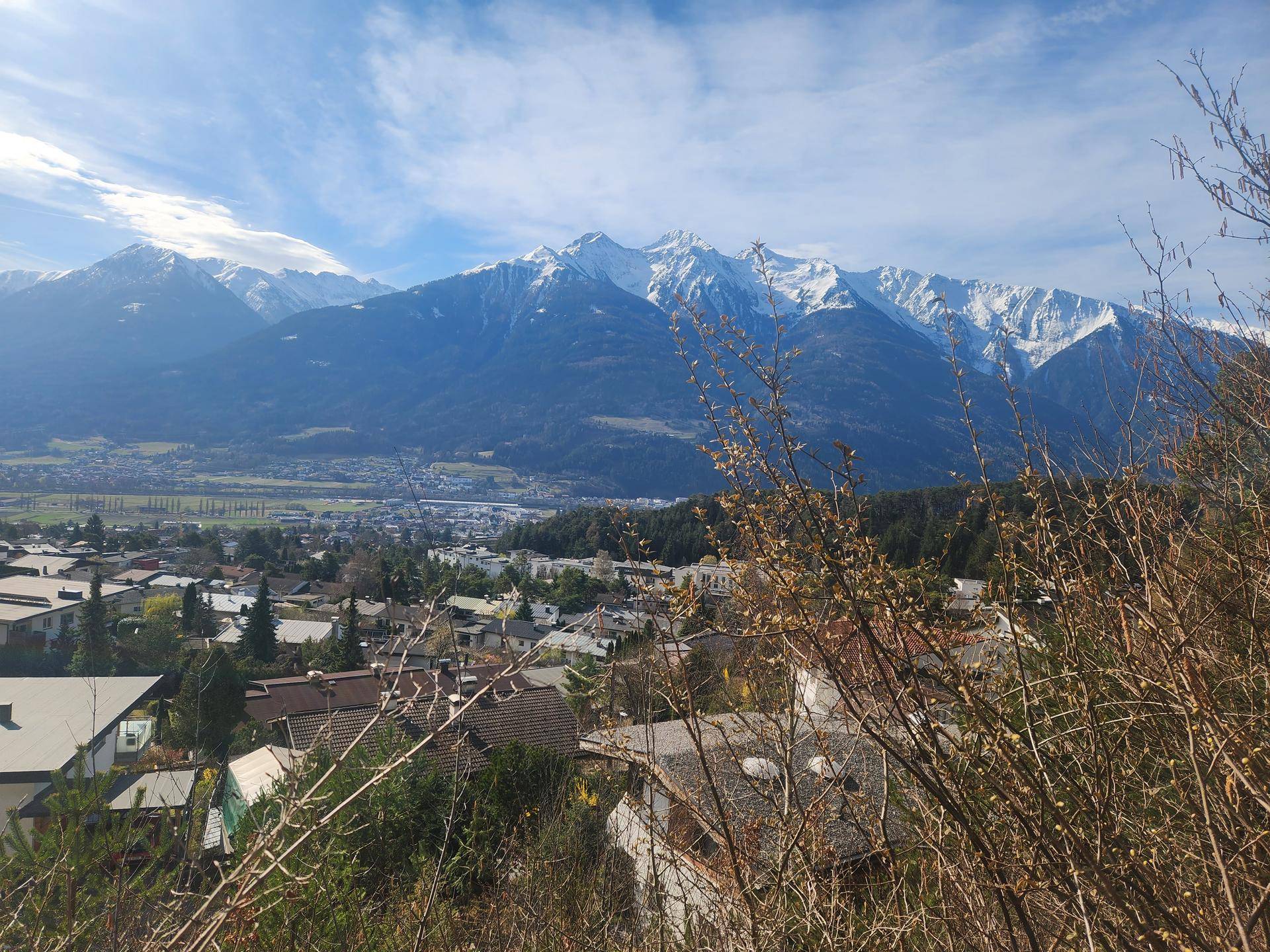 Weitläufiger Ausblick auf eine Berglandschaft mit einem Tal und Siedlungen unter blauem Himmel.