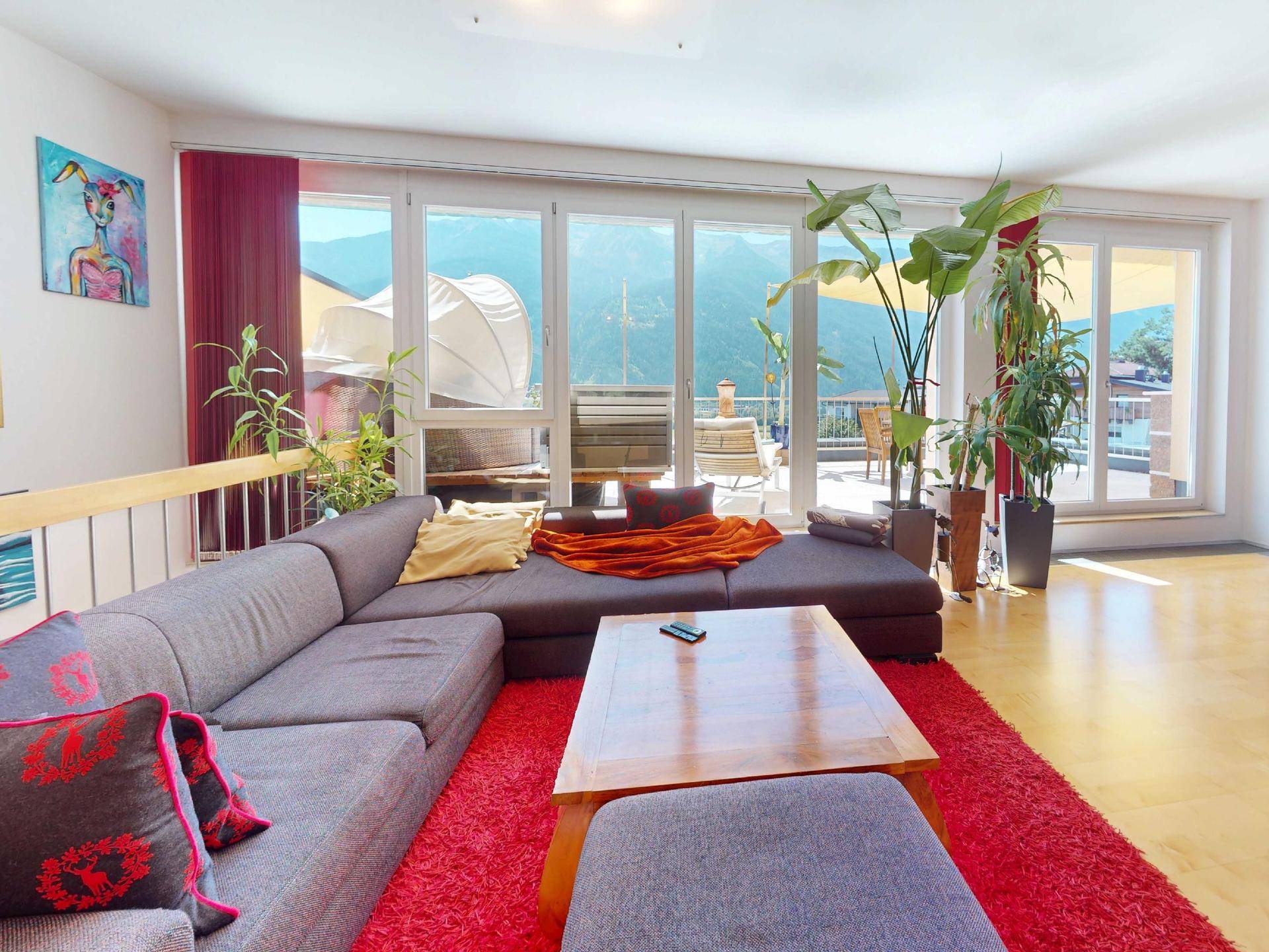 Helles Wohnzimmer mit großem Sofa, rotem Teppich und Zugang zur Terrasse mit Bergblick.