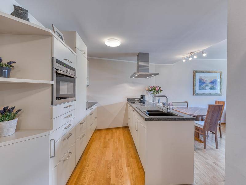 Moderne Einbauküche mit weißen Schränken, dunkler Arbeitsplatte und integrierten Geräten.