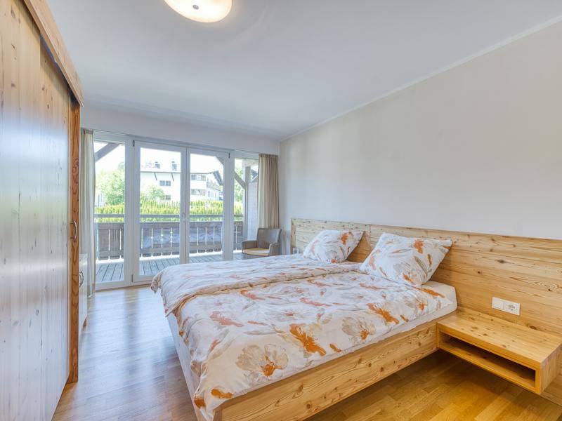 Gemütliches Schlafzimmer mit Holzbett, Parkettboden und großen Fenstern zum Balkon.