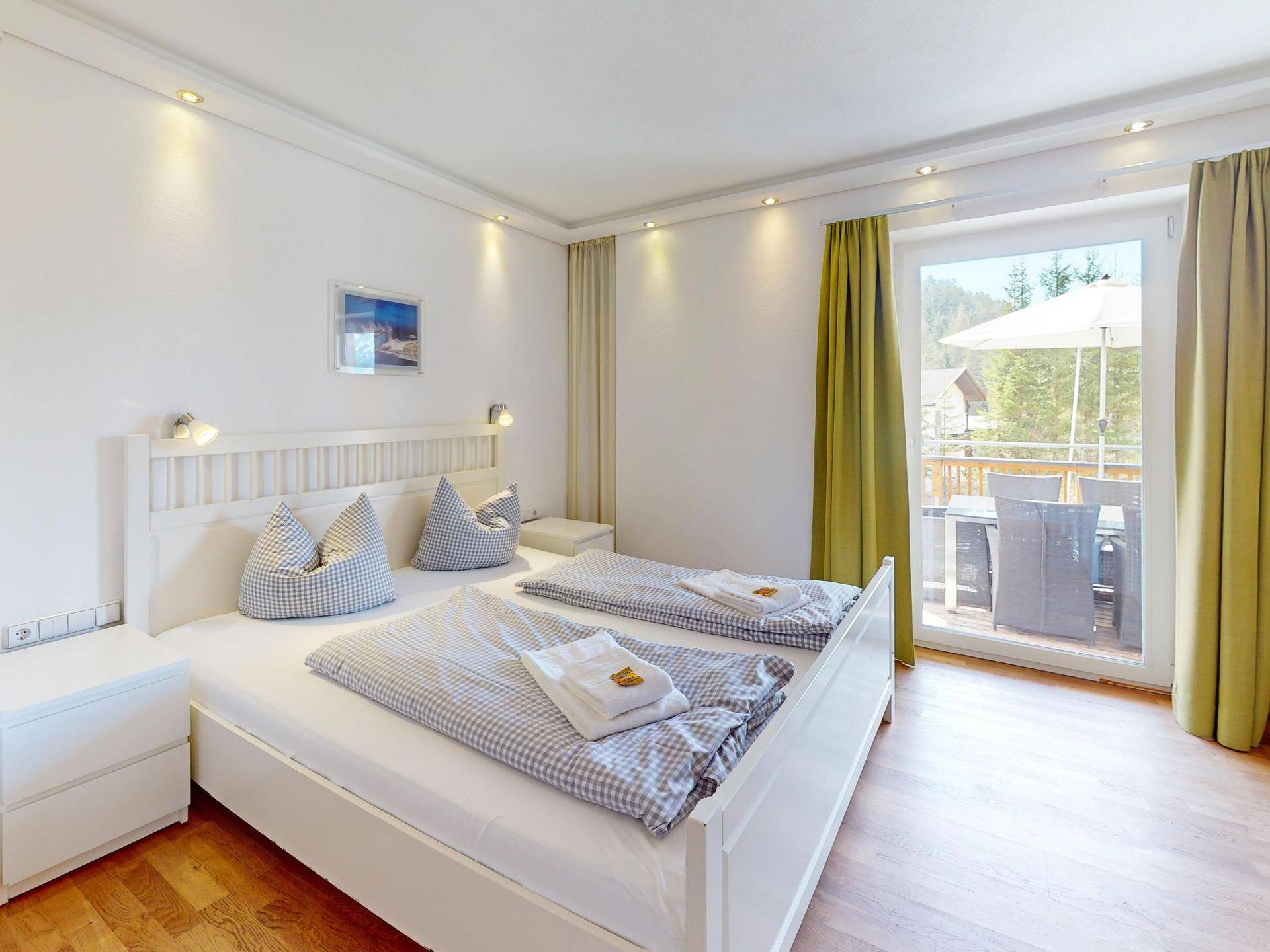 Helles Schlafzimmer mit Doppelbett, Holzboden und direktem Zugang zu einem Balkon oder einer Terrasse.