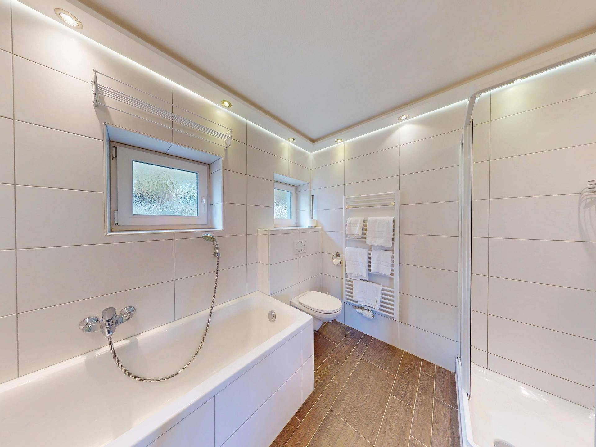 Modernes Badezimmer mit Badewanne, Dusche, WC und Fenster für natürliche Belüftung.