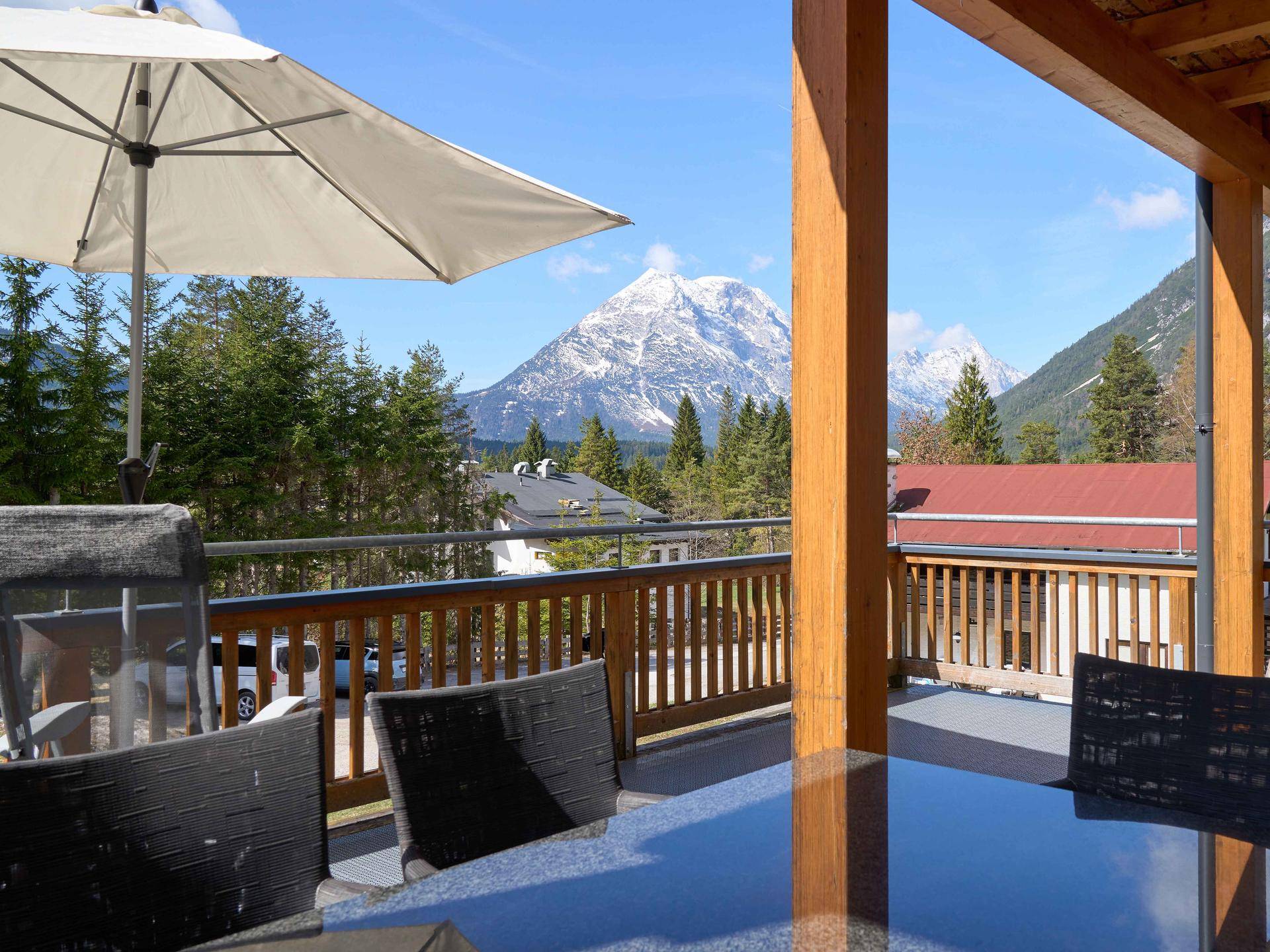 Große Sonnenterrasse mit Esstisch, Sonnenschirm und beeindruckendem Panoramablick auf die Berge.