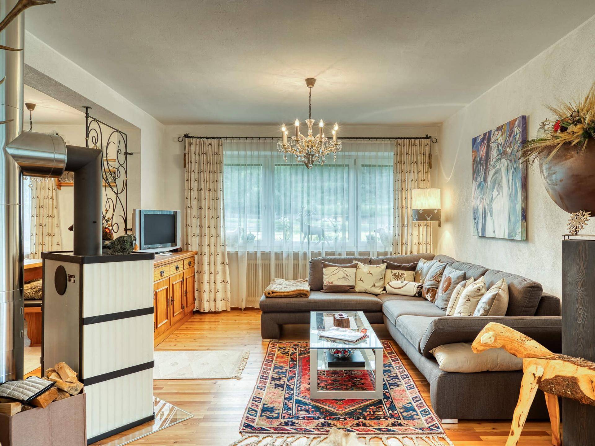 Gemütliches Wohnzimmer im alpinen Stil mit Kaminofen, Holzboden und großem Sofa.