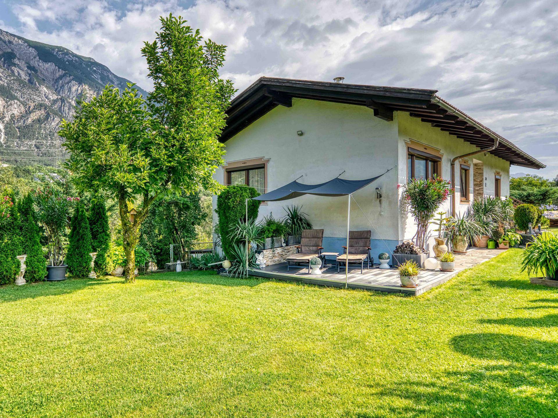 Großer Garten mit Rasenfläche, Bäumen und einer gemütlichen Terrasse mit Sonnenschutz.