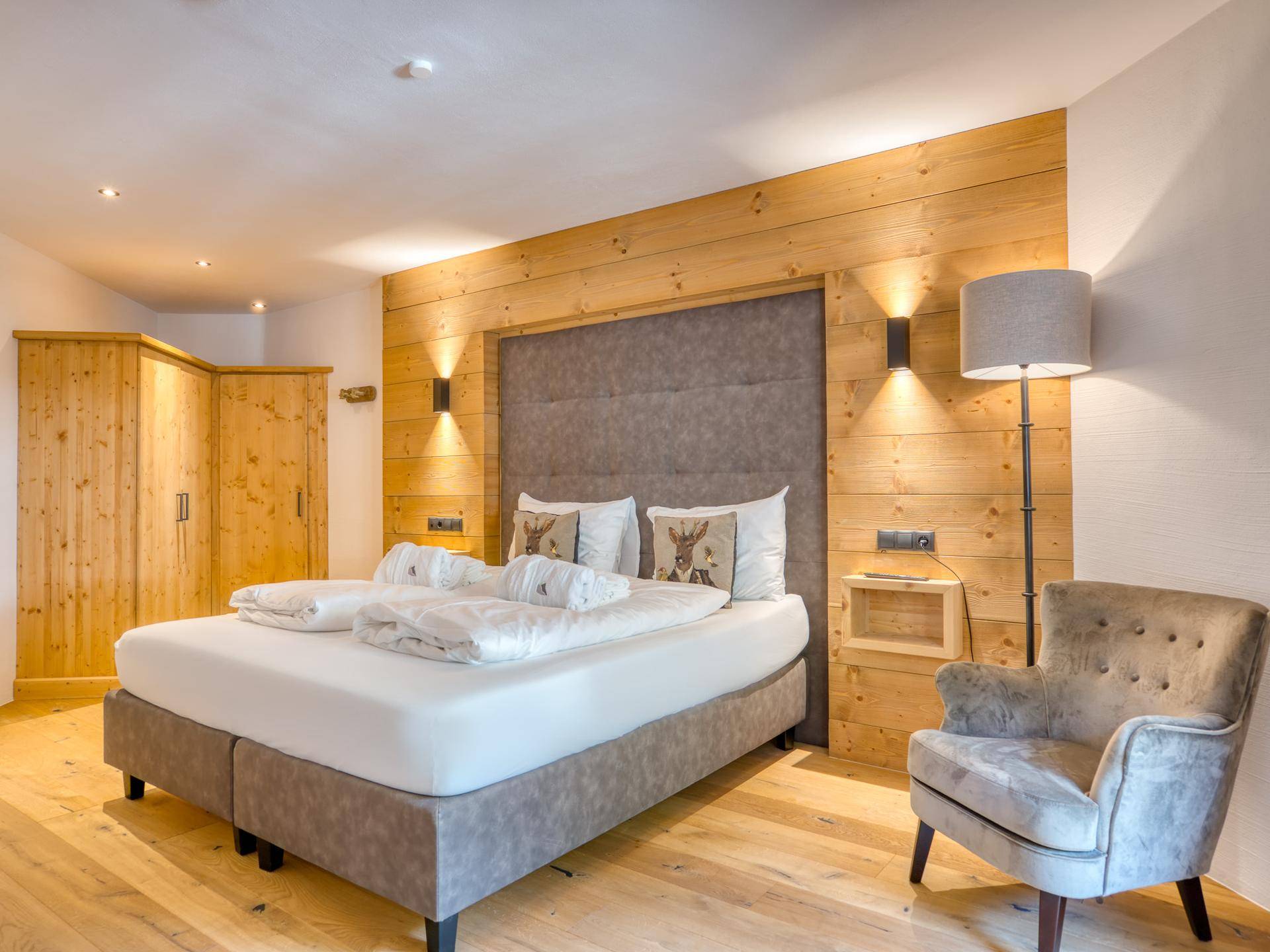 Gemütliches Schlafzimmer im alpinen Stil mit Holzwandverkleidung, Doppelbett und bequemen Sessel.