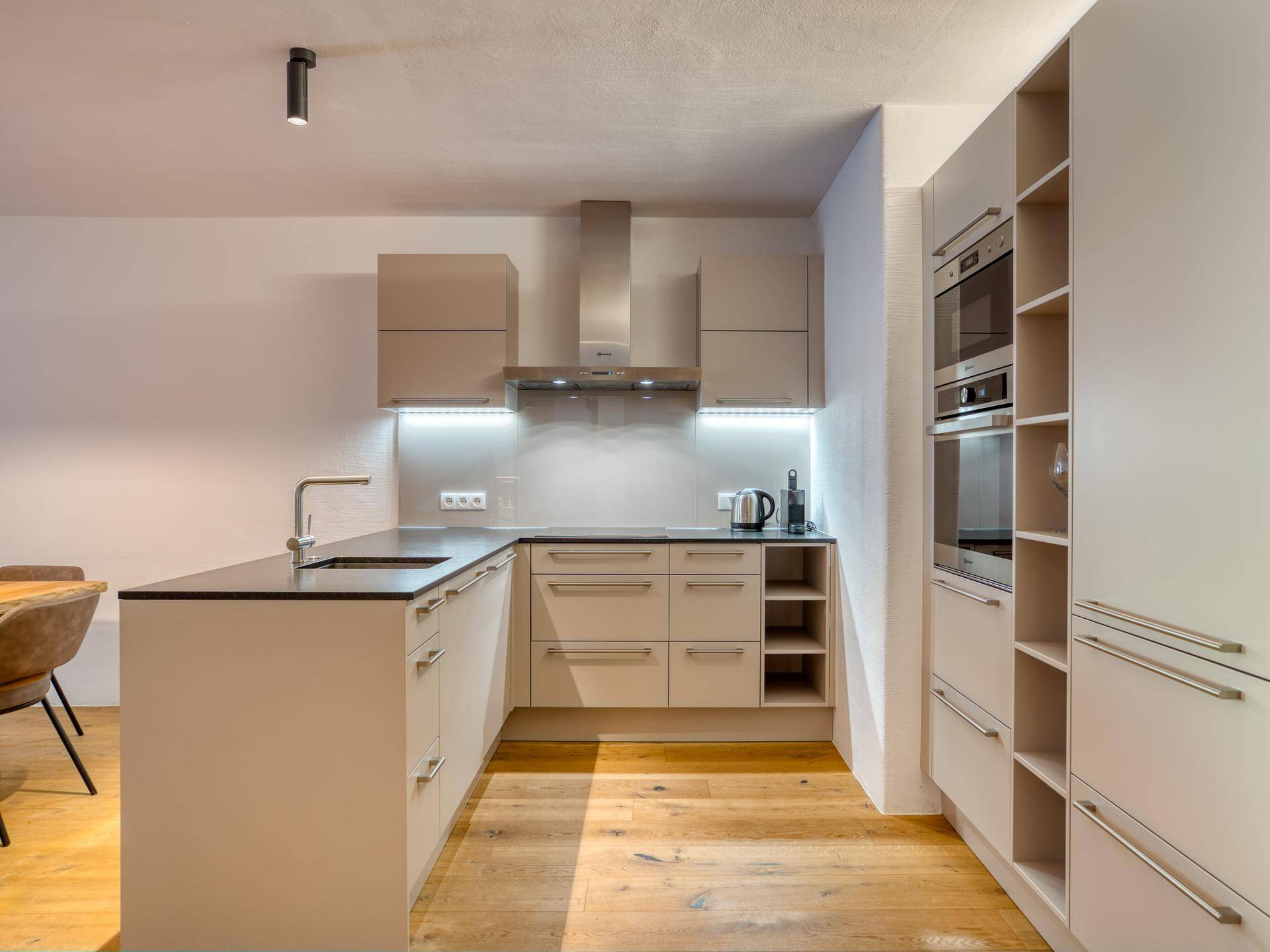 Moderne Einbauküche mit hellen Schränken, dunkler Arbeitsplatte und integrierten Geräten.