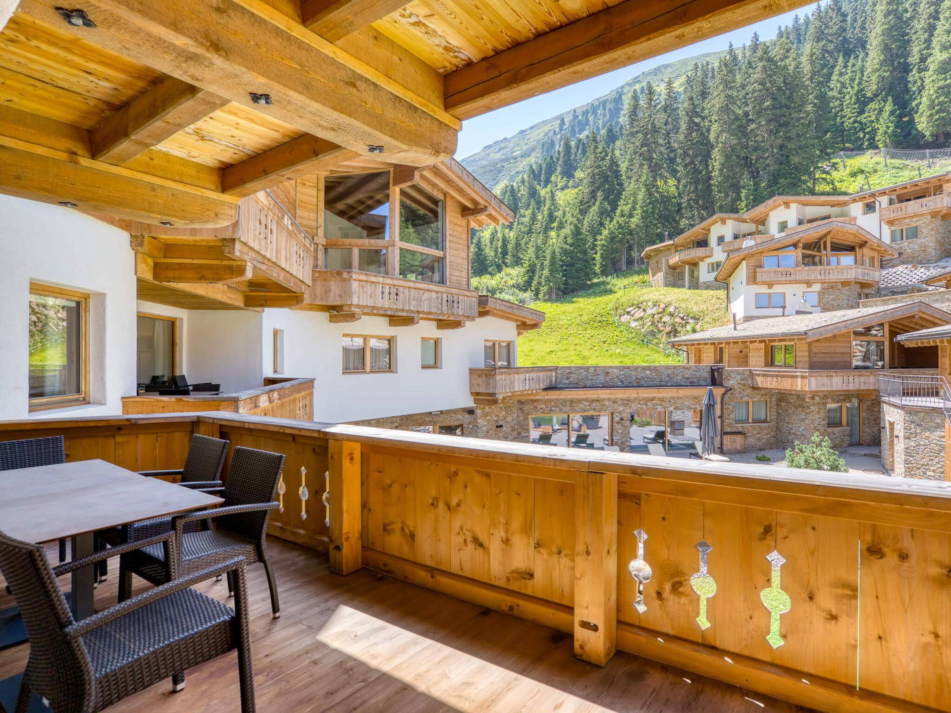 Großer Holzbalkon mit Sitzgelegenheiten und Panoramablick auf die umliegenden Berge und Chalets.