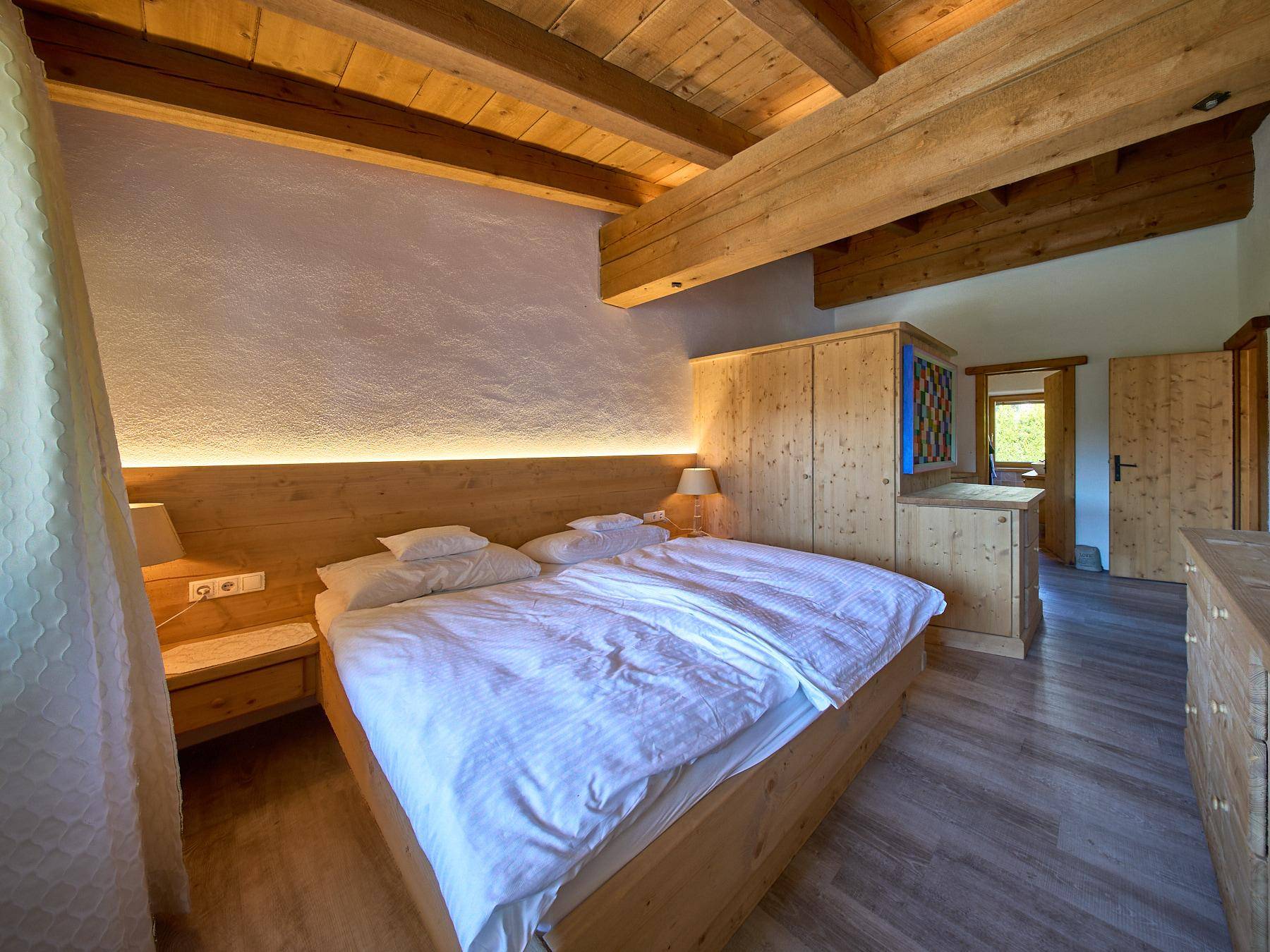 Schlafzimmer im alpinen Stil mit Holzbett, Holzbalkendecke und indirekter Beleuchtung.