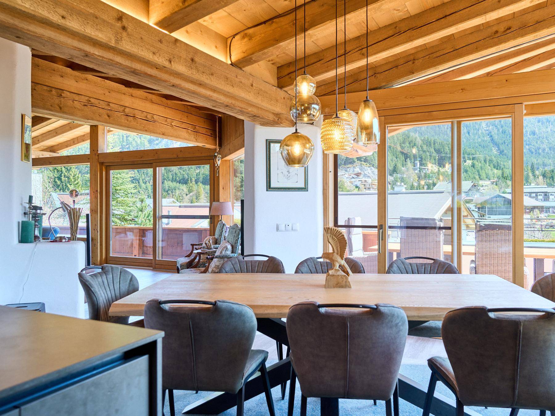 Heller Essbereich mit Holztisch, modernen Hängelampen und Zugang zum Balkon mit Bergblick.