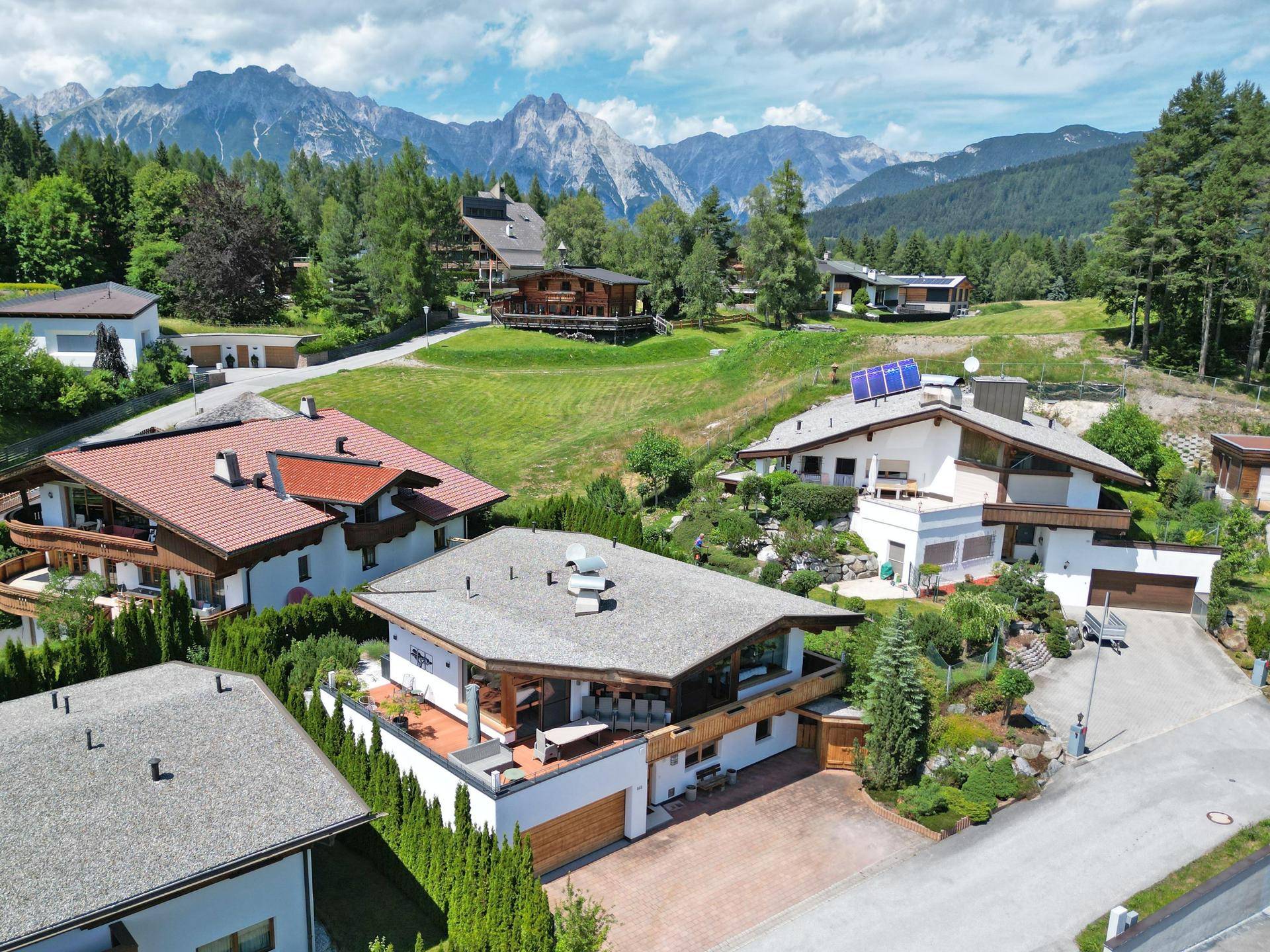 Luftaufnahme einer Wohnsiedlung in den Bergen mit mehreren Häusern und grüner Umgebung.