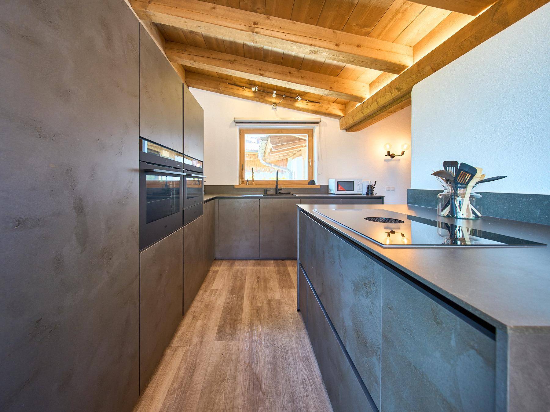 Moderne Küche mit dunklen Fronten, Holzbalkendecke und integrierten Geräten.