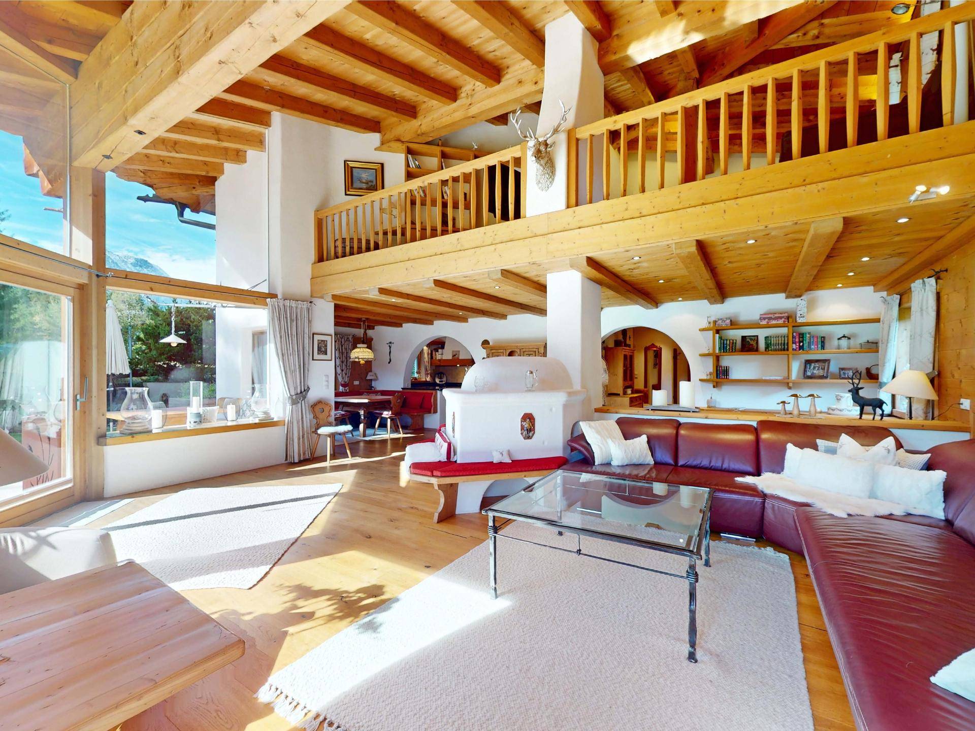 Geräumiges Wohnzimmer mit Galerie, Ledersofa, Kachelofen und traditionellen Holzelementen.