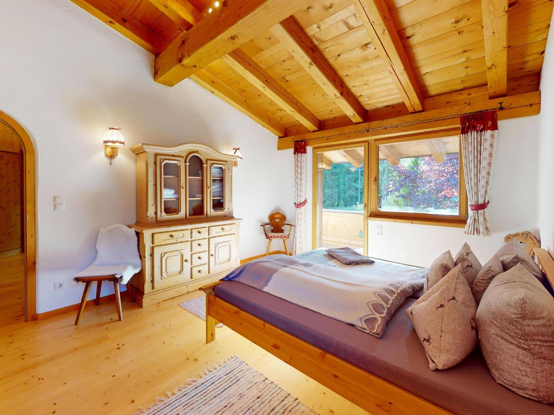 Schlafzimmer im alpinen Stil mit Holzbalkendecke, traditionellen Möbeln und Zugang zum Balkon.