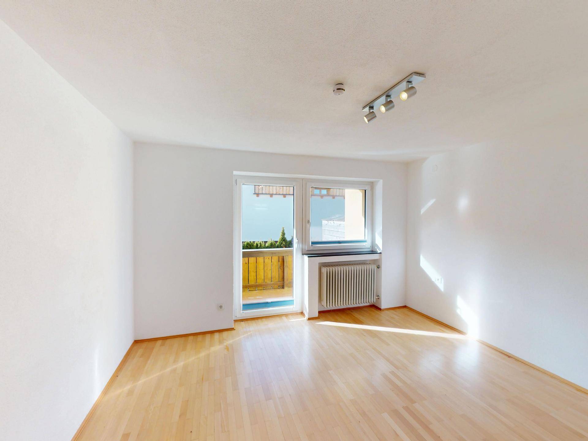 Helles Zimmer mit Holzboden, Heizkörper und direktem Zugang zum Balkon.