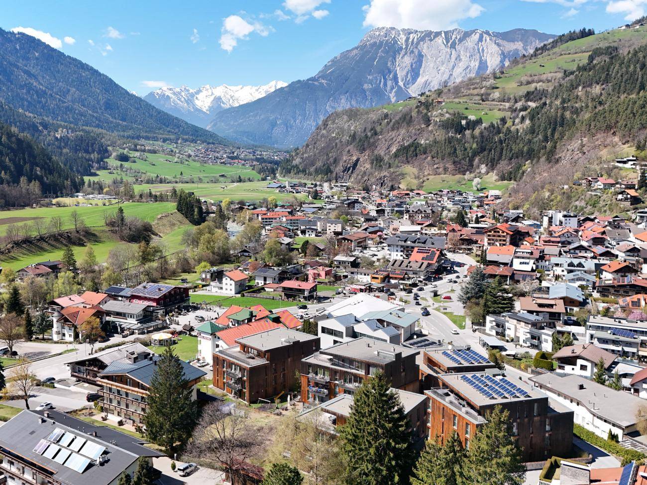 Panoramablick auf eine malerische Stadt im Tal, umgeben von majestätischen Bergen und grünen Hängen.