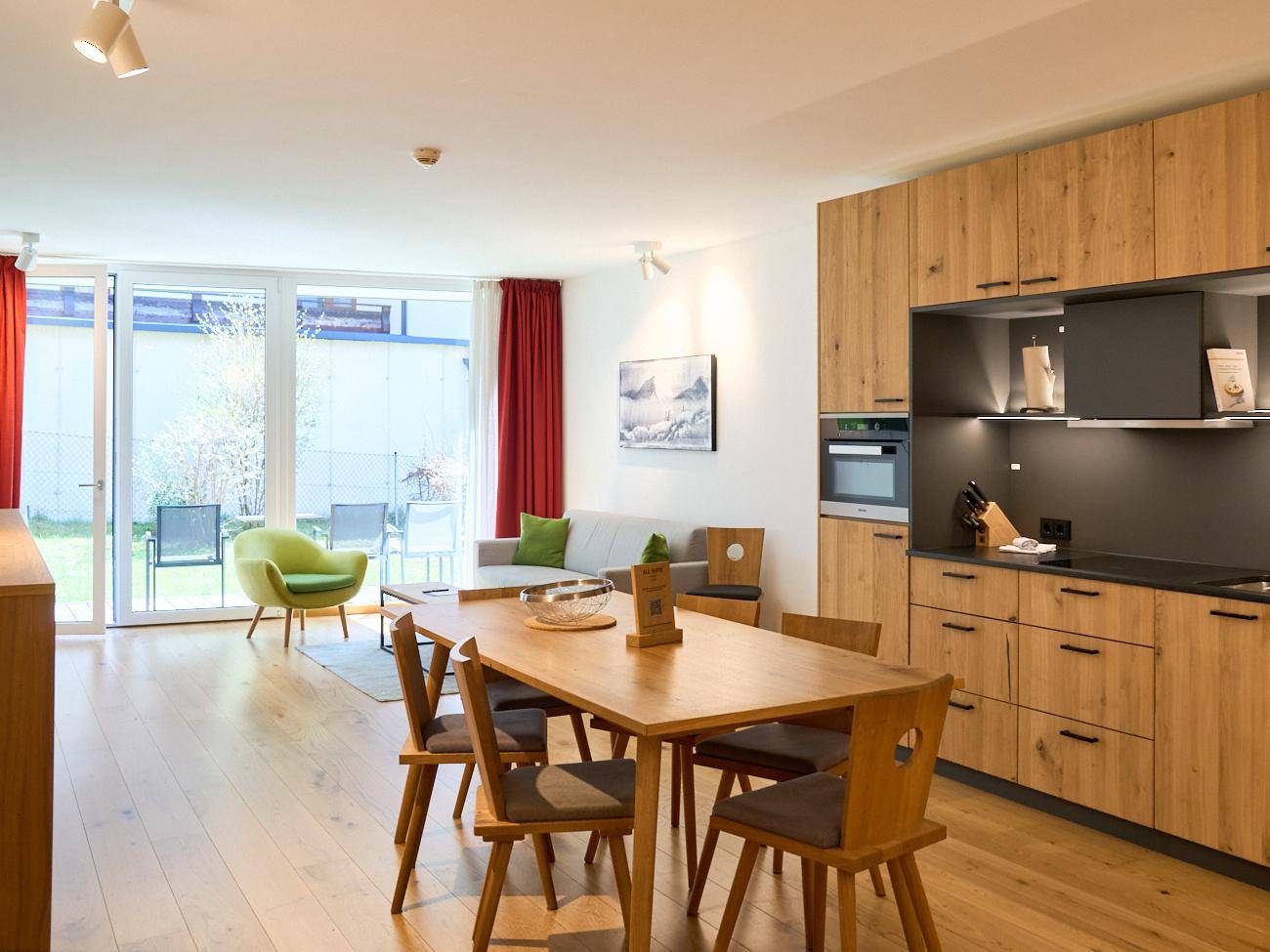 Heller offener Wohn-Essbereich mit moderner Holzküche, Parkettboden und Zugang zur Terrasse.
