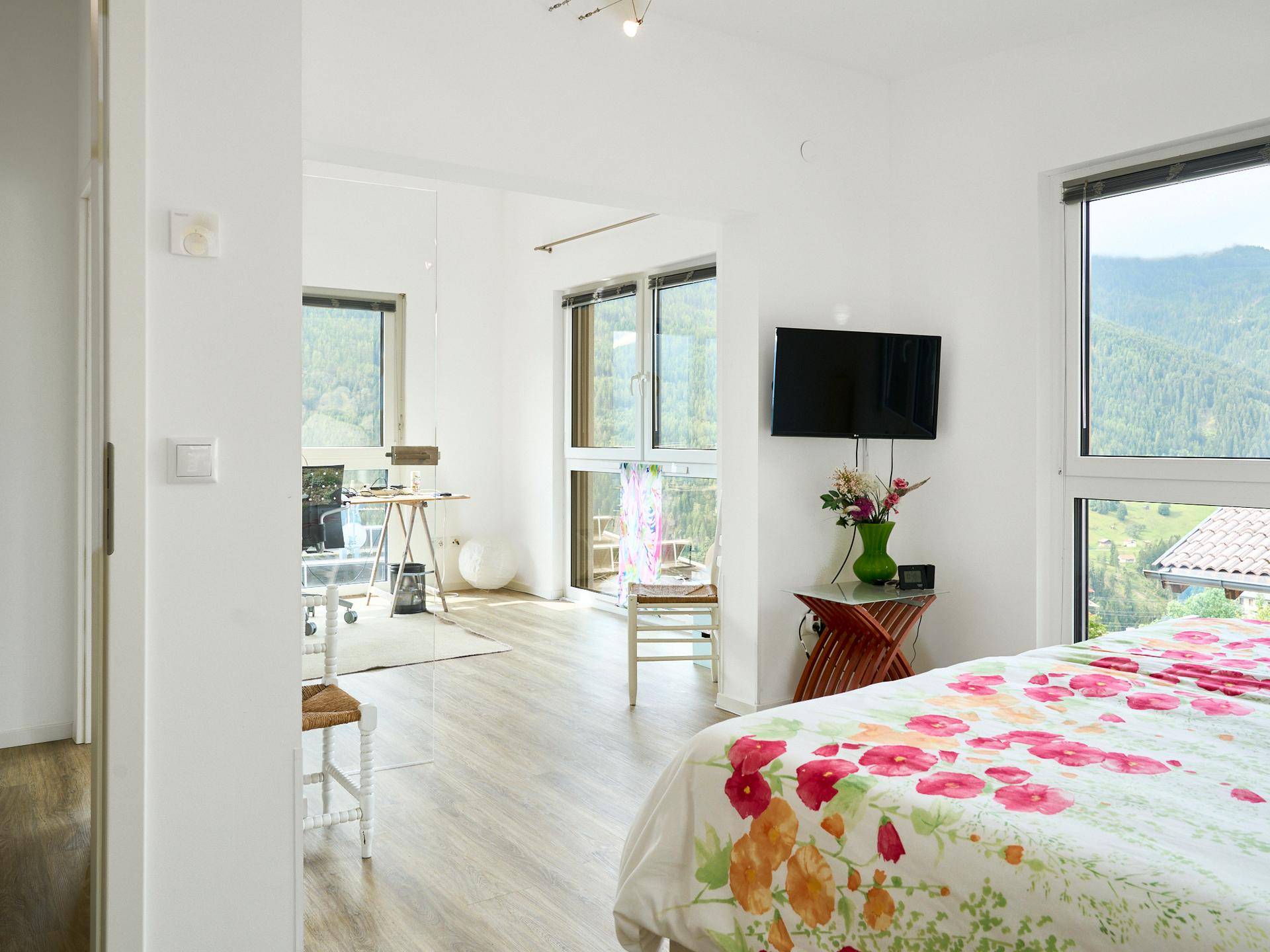 Helles Schlafzimmer mit floraler Bettwäsche und Panoramablick auf die umliegende Berglandschaft.