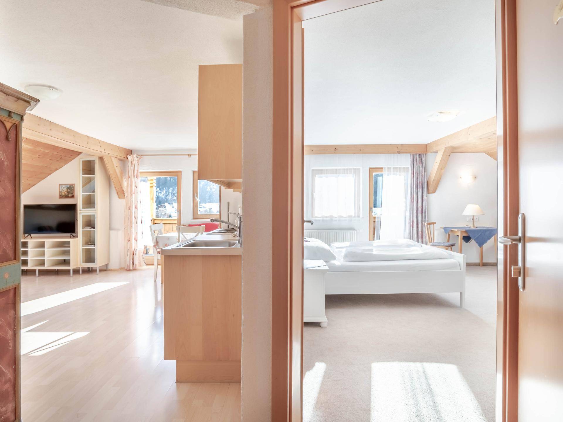 Blick durch eine Tür in einen offenen Wohnbereich mit Küche und angrenzendem Schlafzimmer.