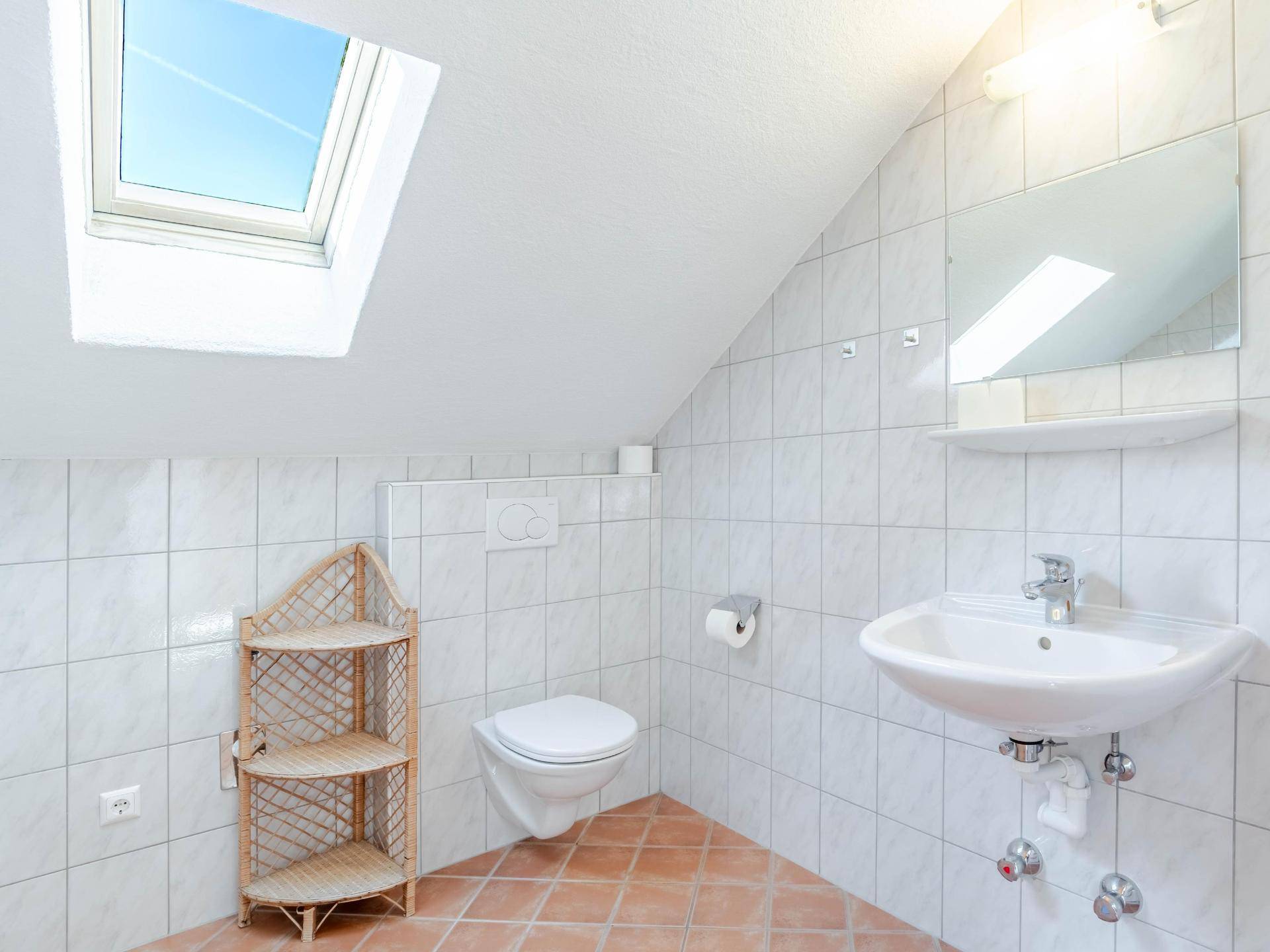 Badezimmer im Dachgeschoss mit Dachfenster, WC, Waschbecken und hellen Fliesen.