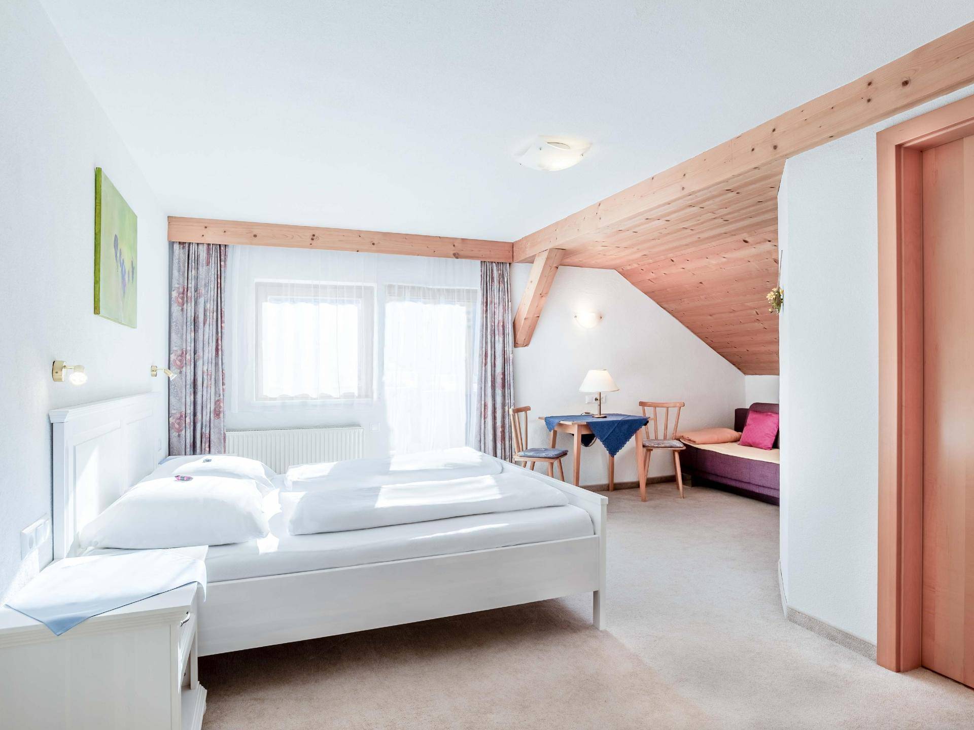 Helles Schlafzimmer mit Doppelbett, Sitzbereich und Blick auf die umliegende Landschaft.