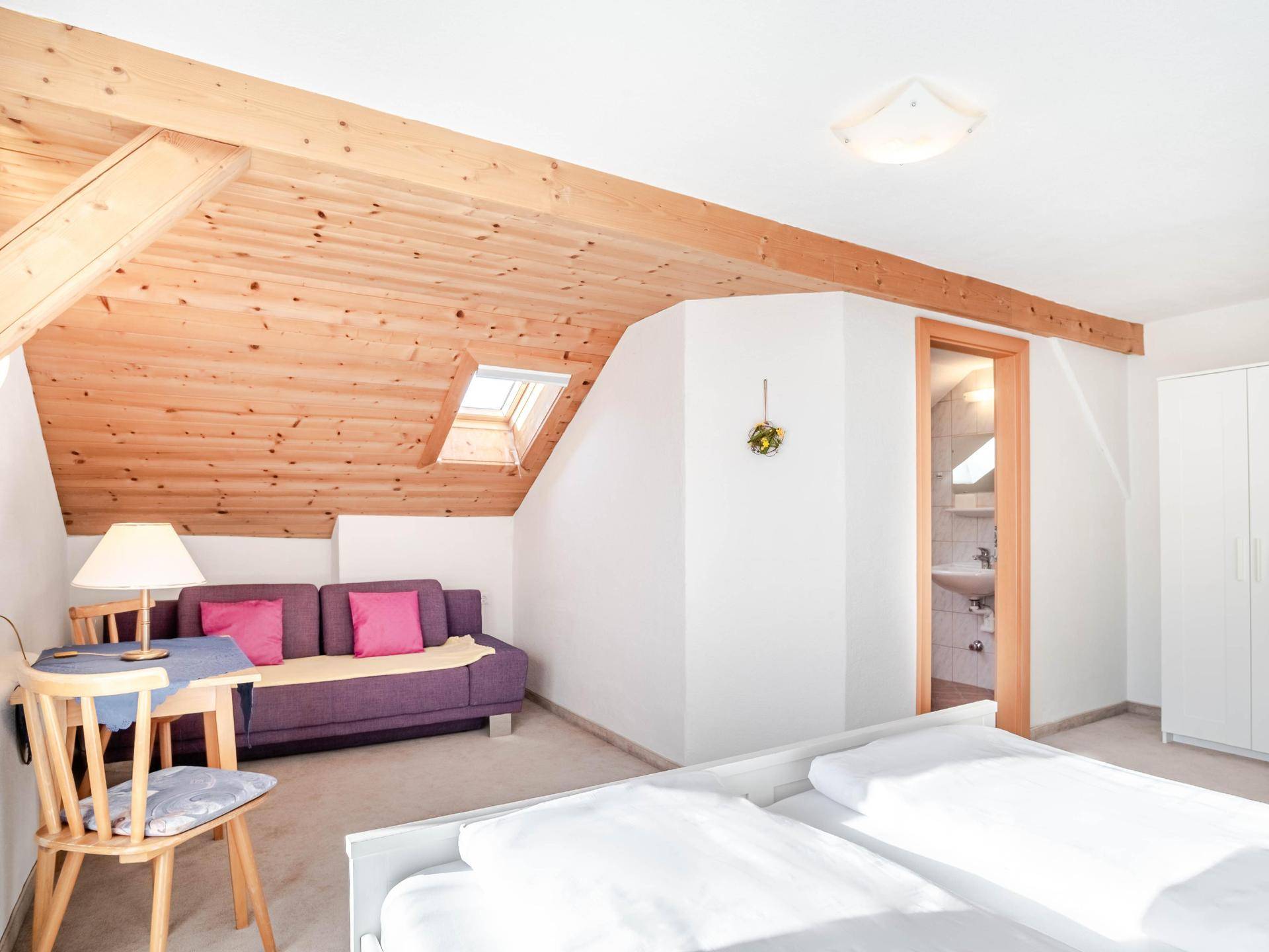 Schlafzimmer im Dachgeschoss mit Doppelbett, Sofa, Holzbalken und Zugang zum Badezimmer.