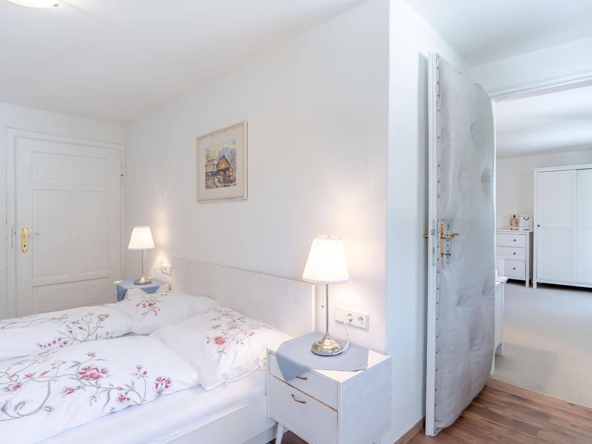 Helles Schlafzimmer mit zwei Einzelbetten, Nachttischen und Blick in einen angrenzenden Raum.