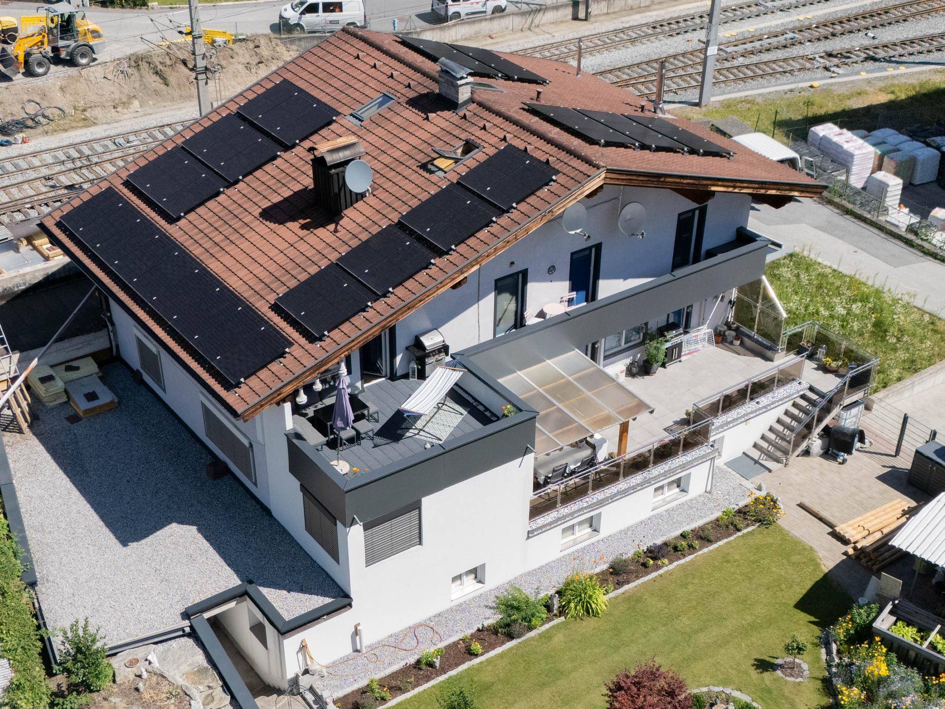 Luftaufnahme eines Hauses mit Photovoltaikanlage, großzügiger Terrasse und gepflegtem Garten.