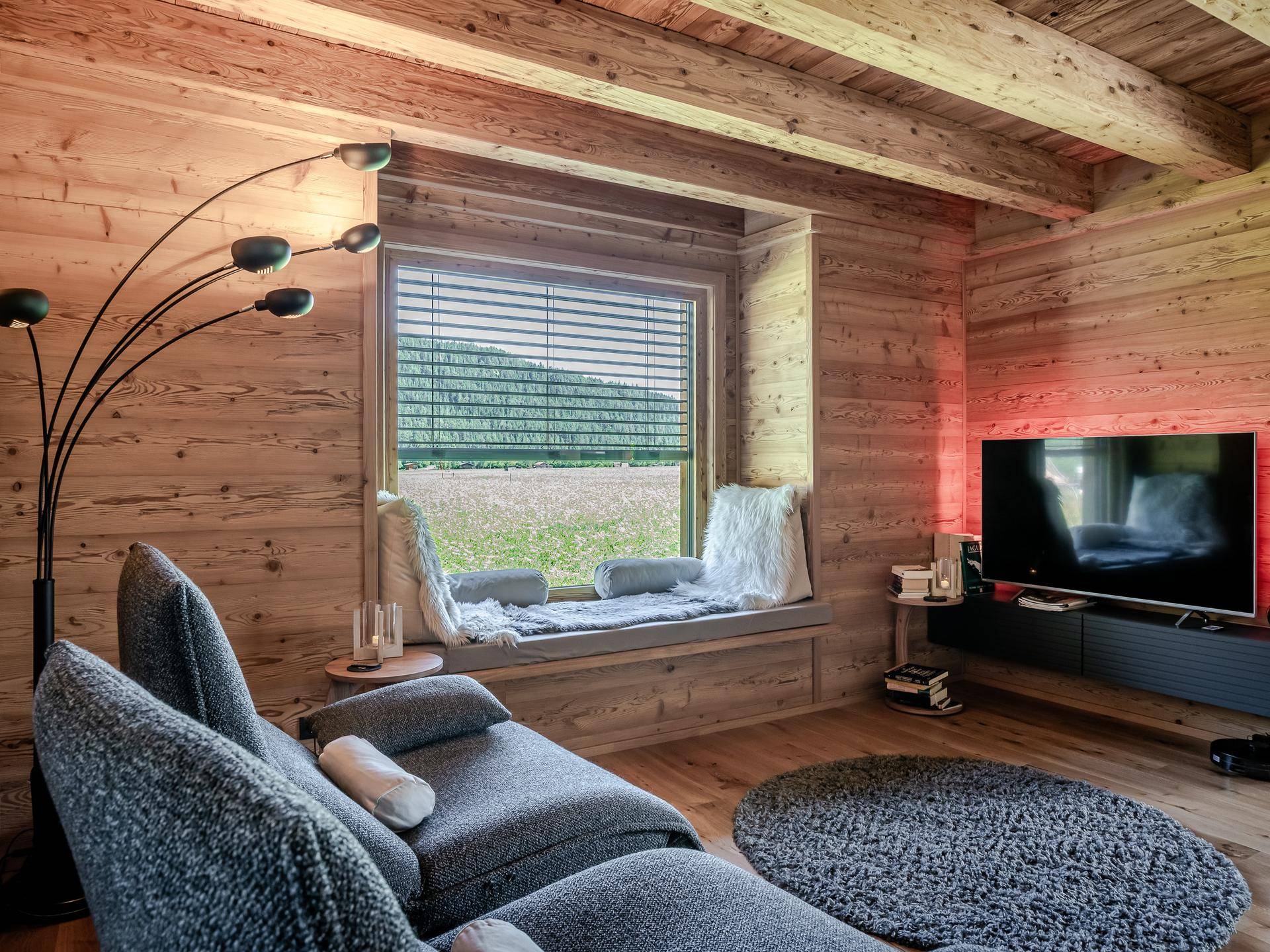 Gemütlicher Wohnbereich mit Holzwänden, bequemen Liegesesseln und einer breiten Fensterbank mit Blick auf die Natur.