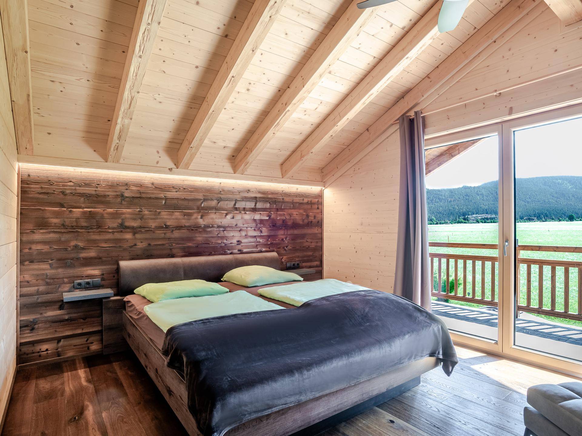 Helles Schlafzimmer mit Holzwänden, hohen Decken und direktem Zugang zu einem Balkon mit Bergblick.