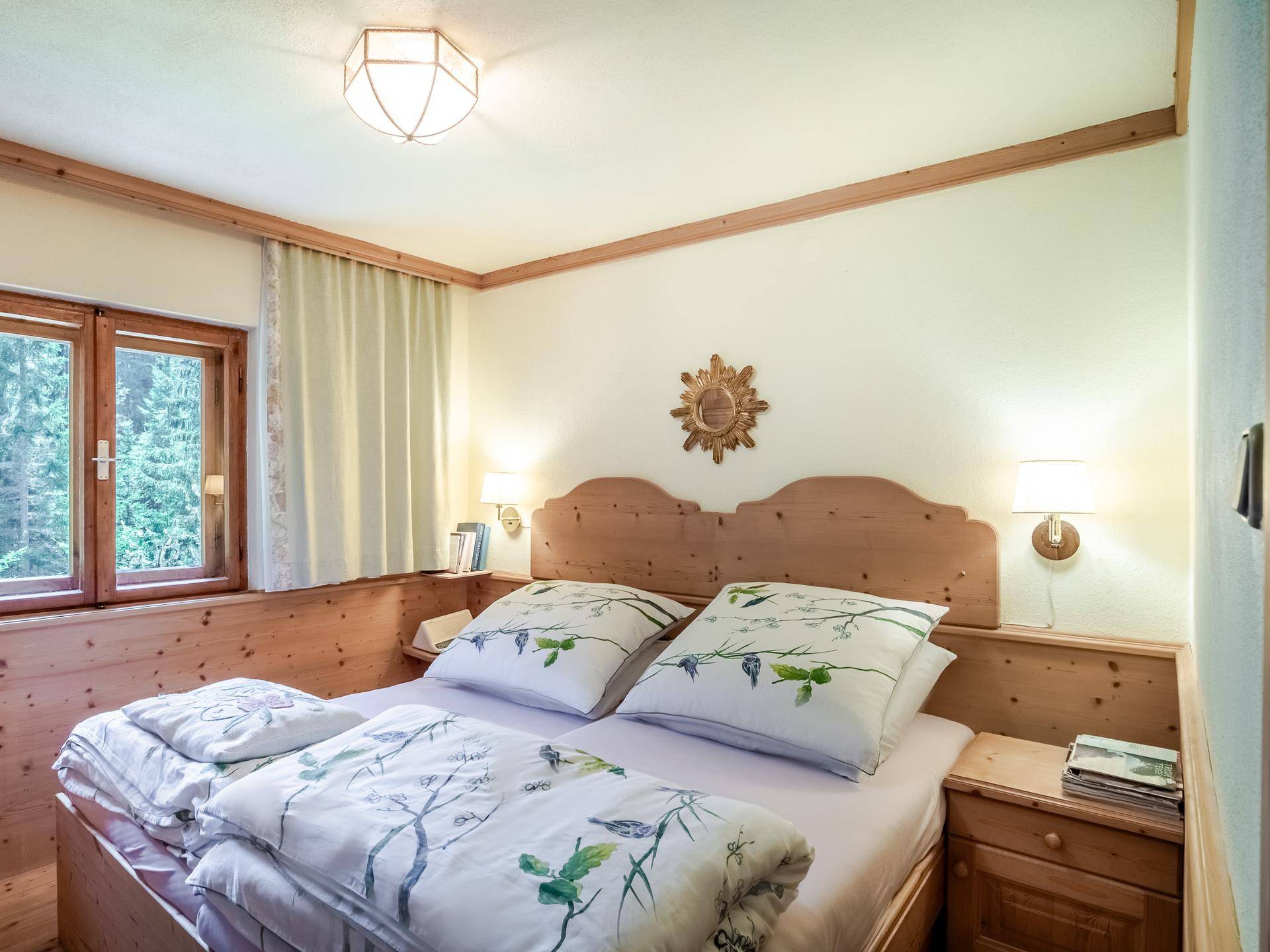 Schlafzimmer im alpinen Stil mit Holzbett, Holzvertäfelung und Blick in die Natur.