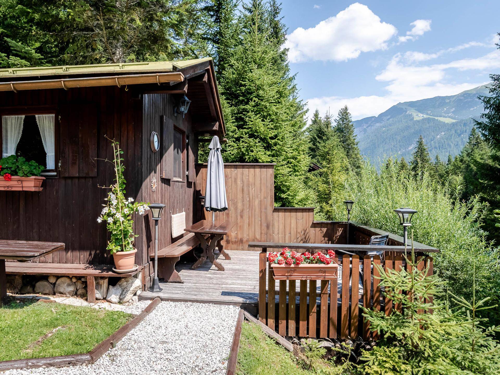 Holzterrasse mit Sitzgelegenheiten, umgeben von Bäumen und mit weitem Bergblick.